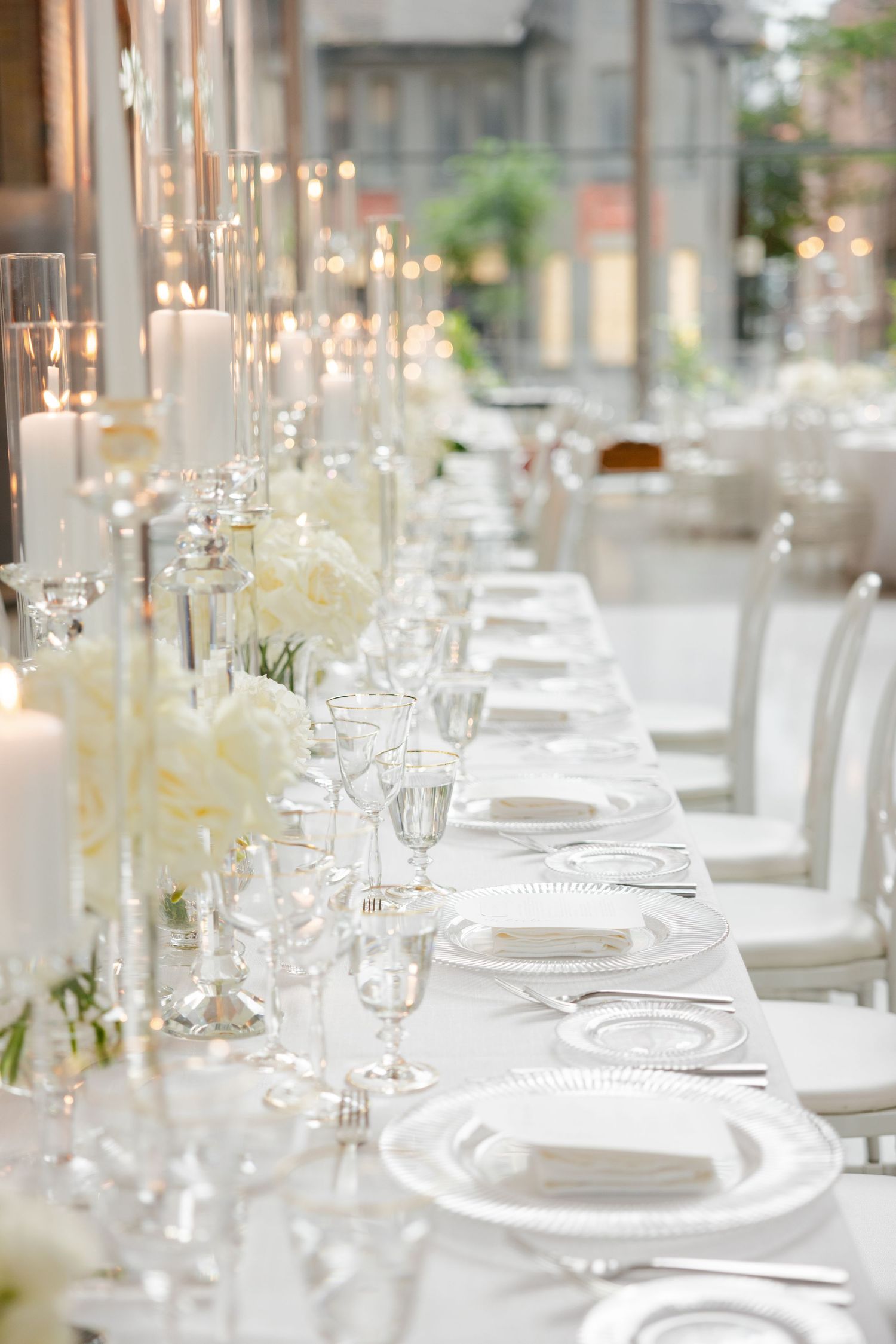 Minimalist white wedding reception table with crystal stemware and candlelit centerpieces.