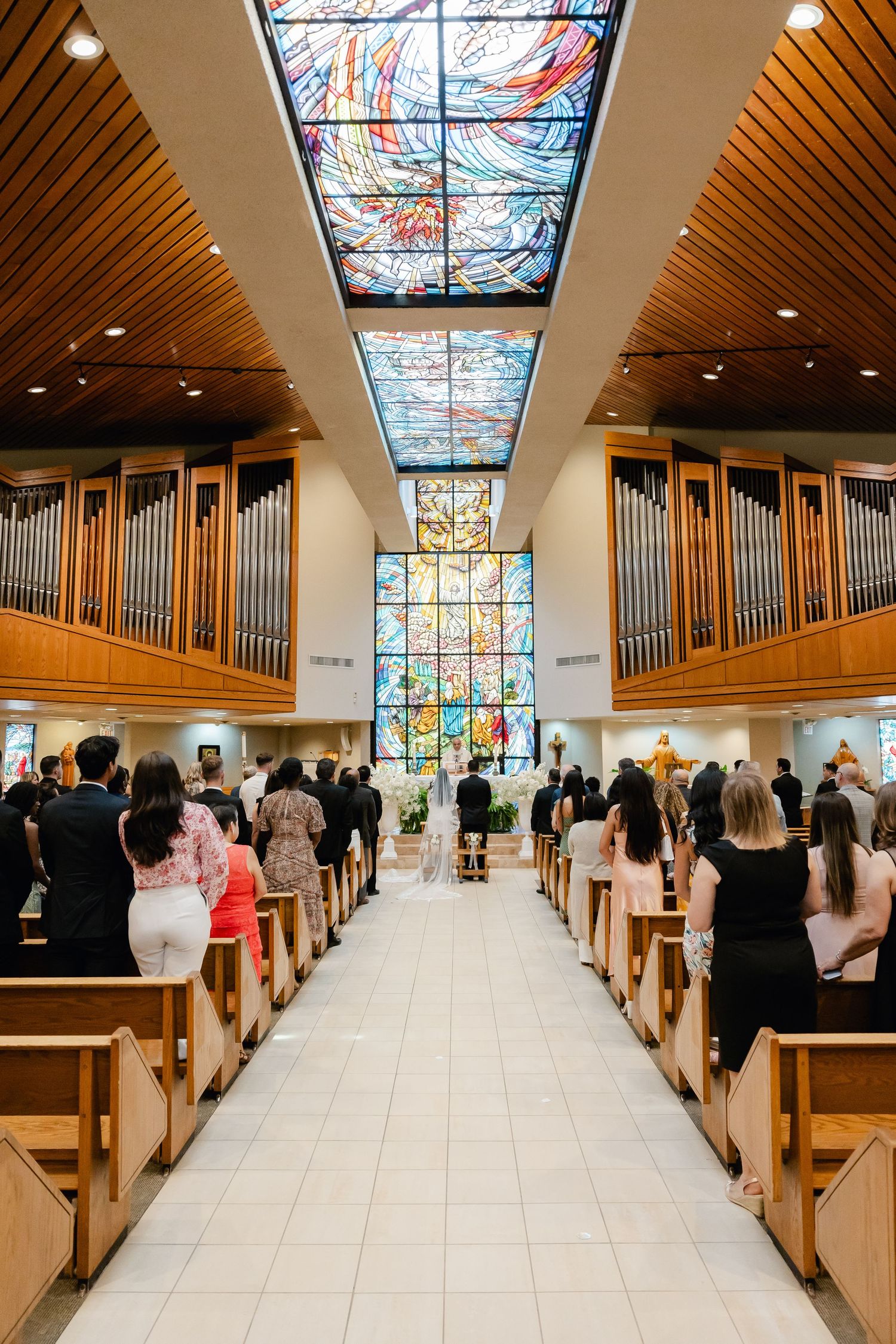 Modern church interior with pipe organs and stained glass skylights during a wedding ceremony.