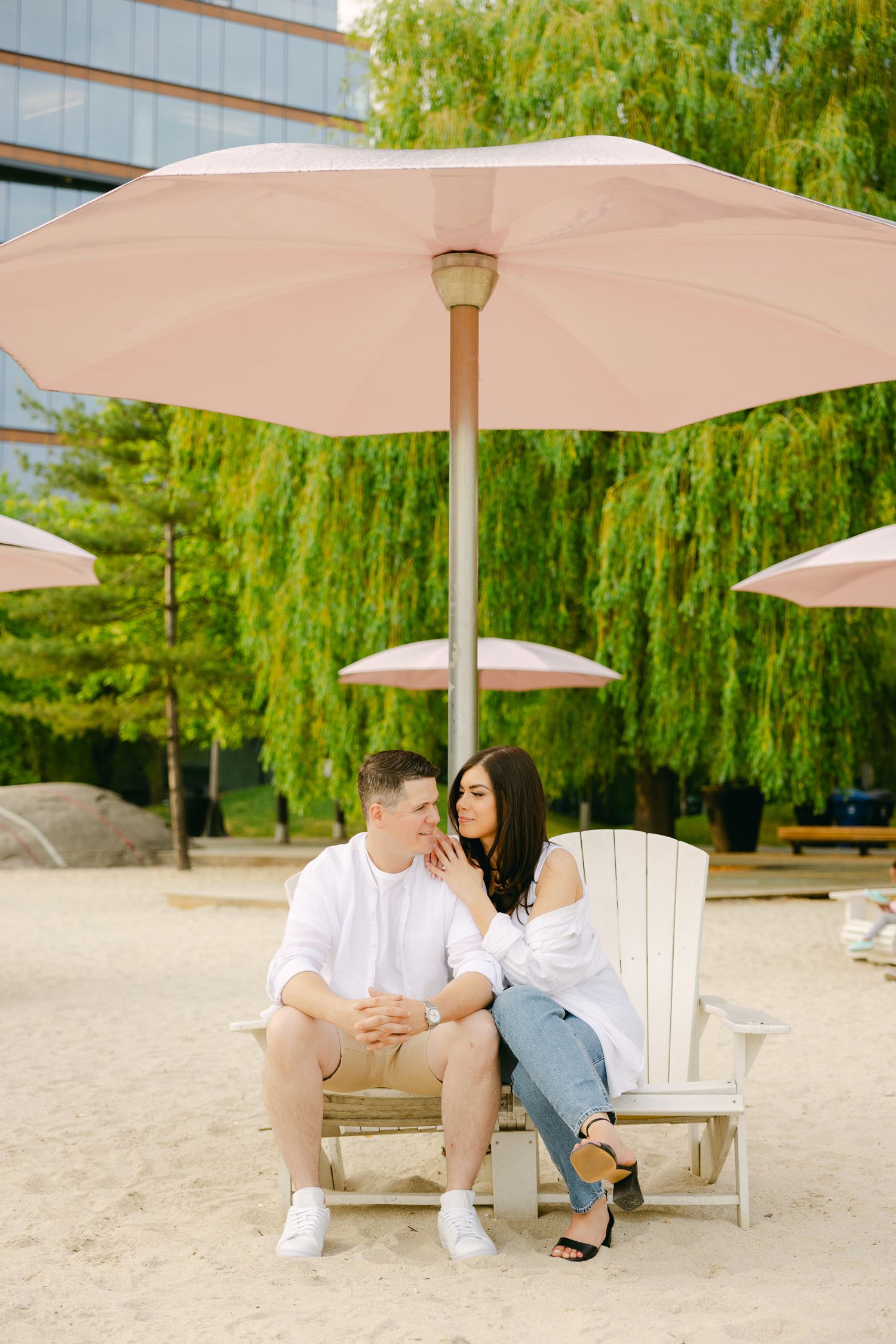 Couple sharing tender moment on Adirondack chair beneath blush pink patio umbrella.