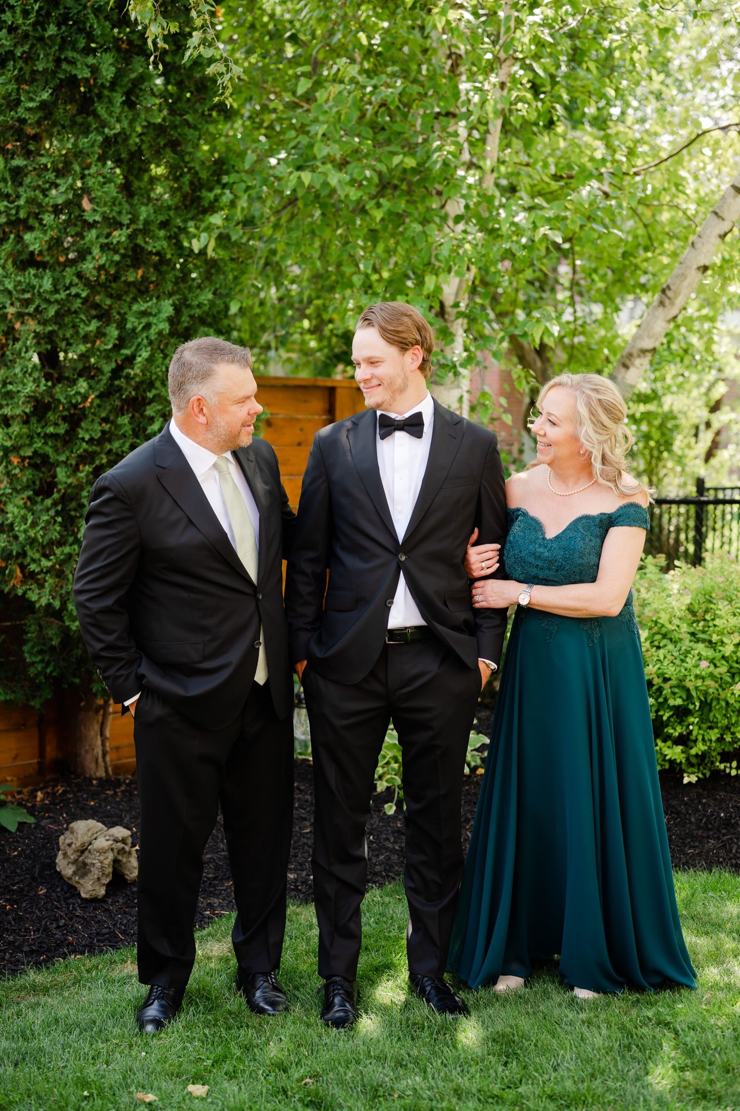 Wedding party members in formal attire conversing in garden setting.