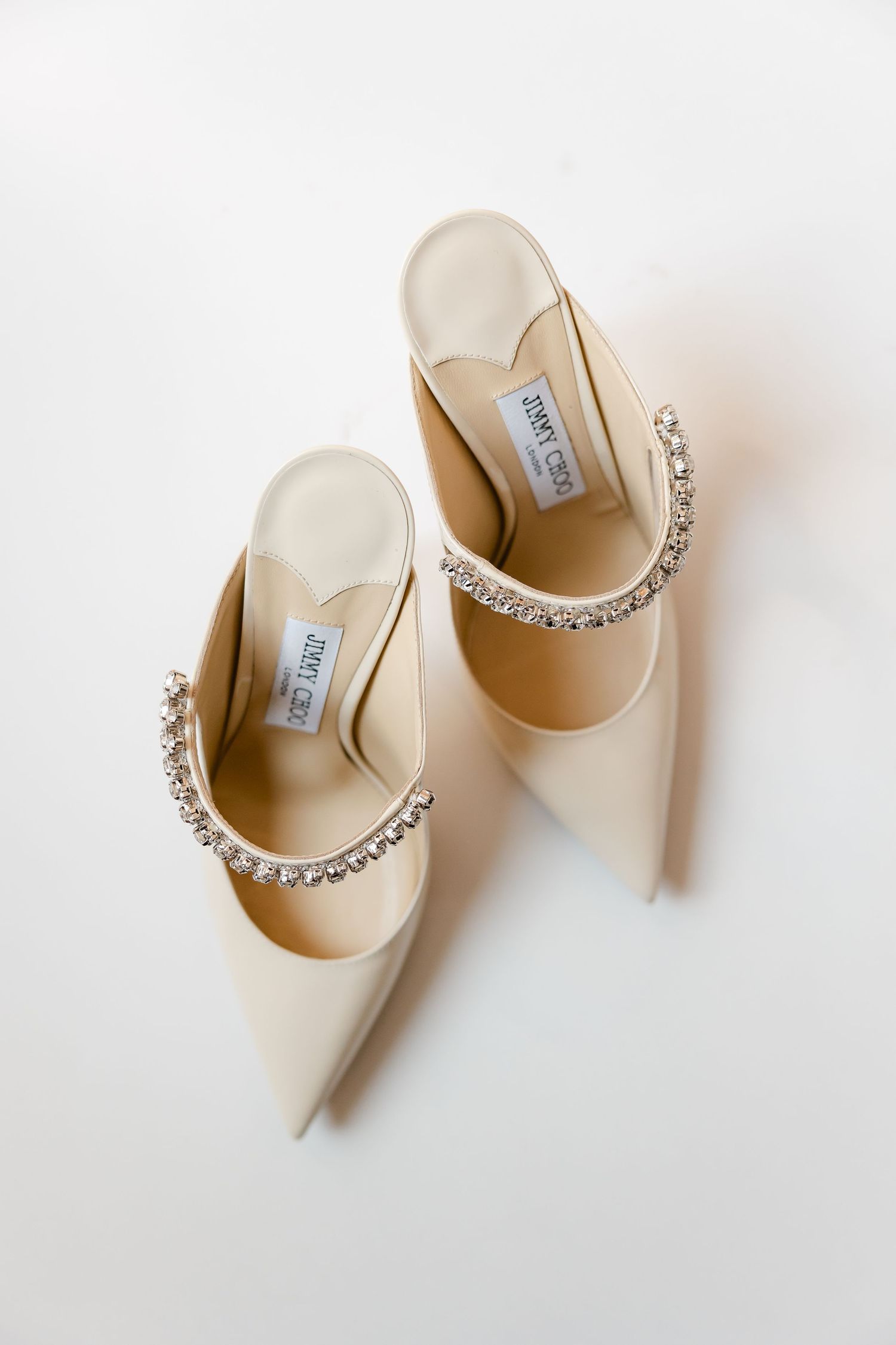 Cream colored bridal mules with crystal embellishments displayed on white background.