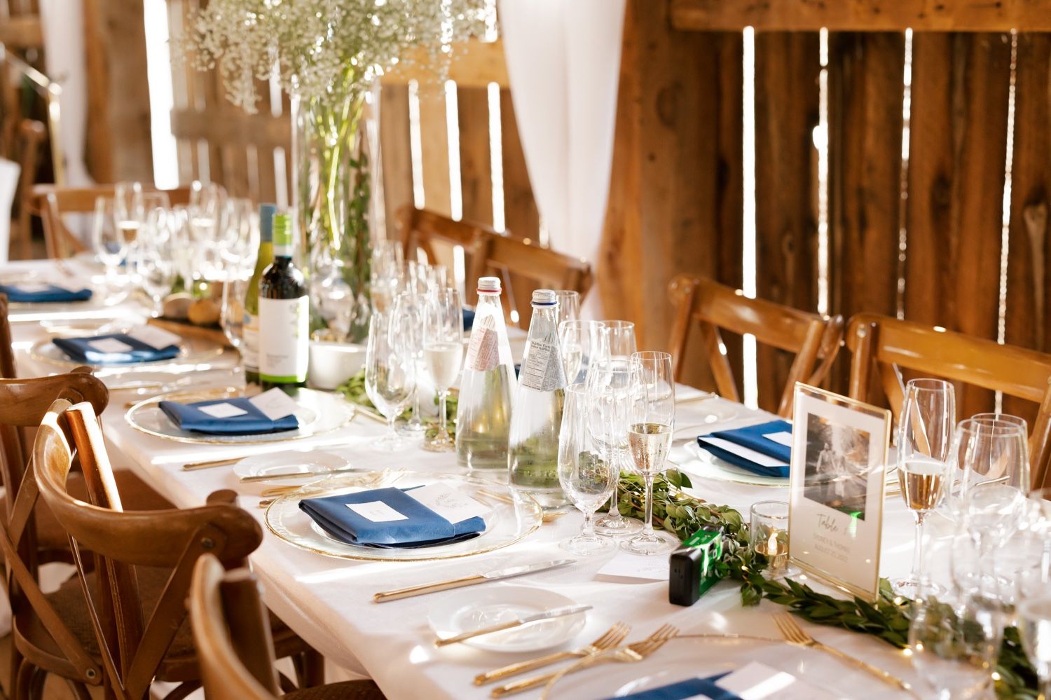 Elegant rustic barn wedding reception table with blue napkins and wine glasses set for dining.
