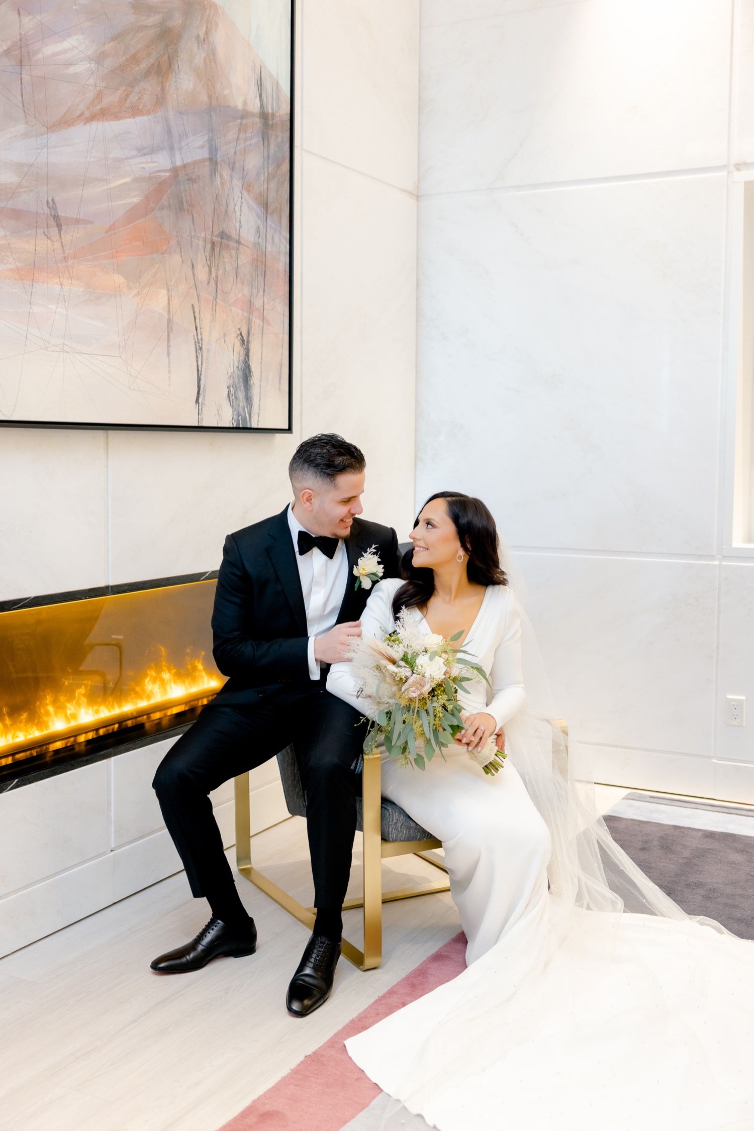 Newlyweds share an intimate moment by a modern fireplace with abstract art and elegant decor.