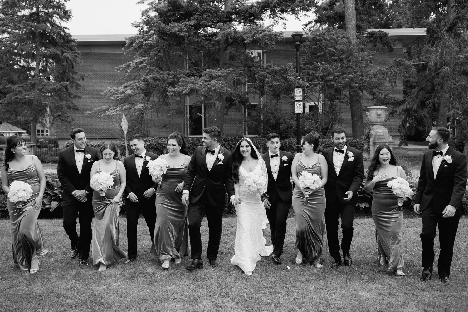 Black and white candid of wedding party walking in sync across a lawn.