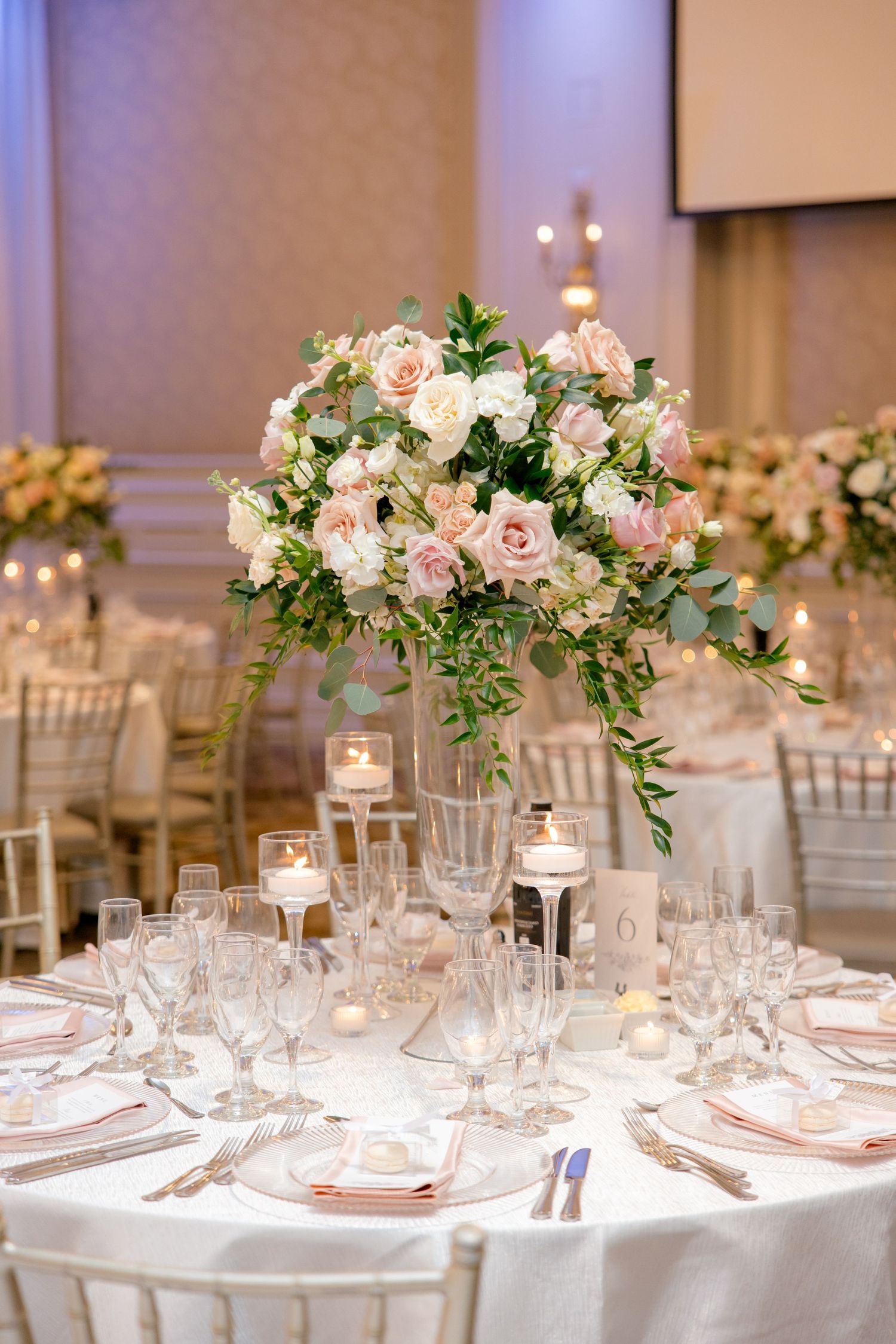 Elegant wedding reception table with tall pink and white floral centerpiece and candles.