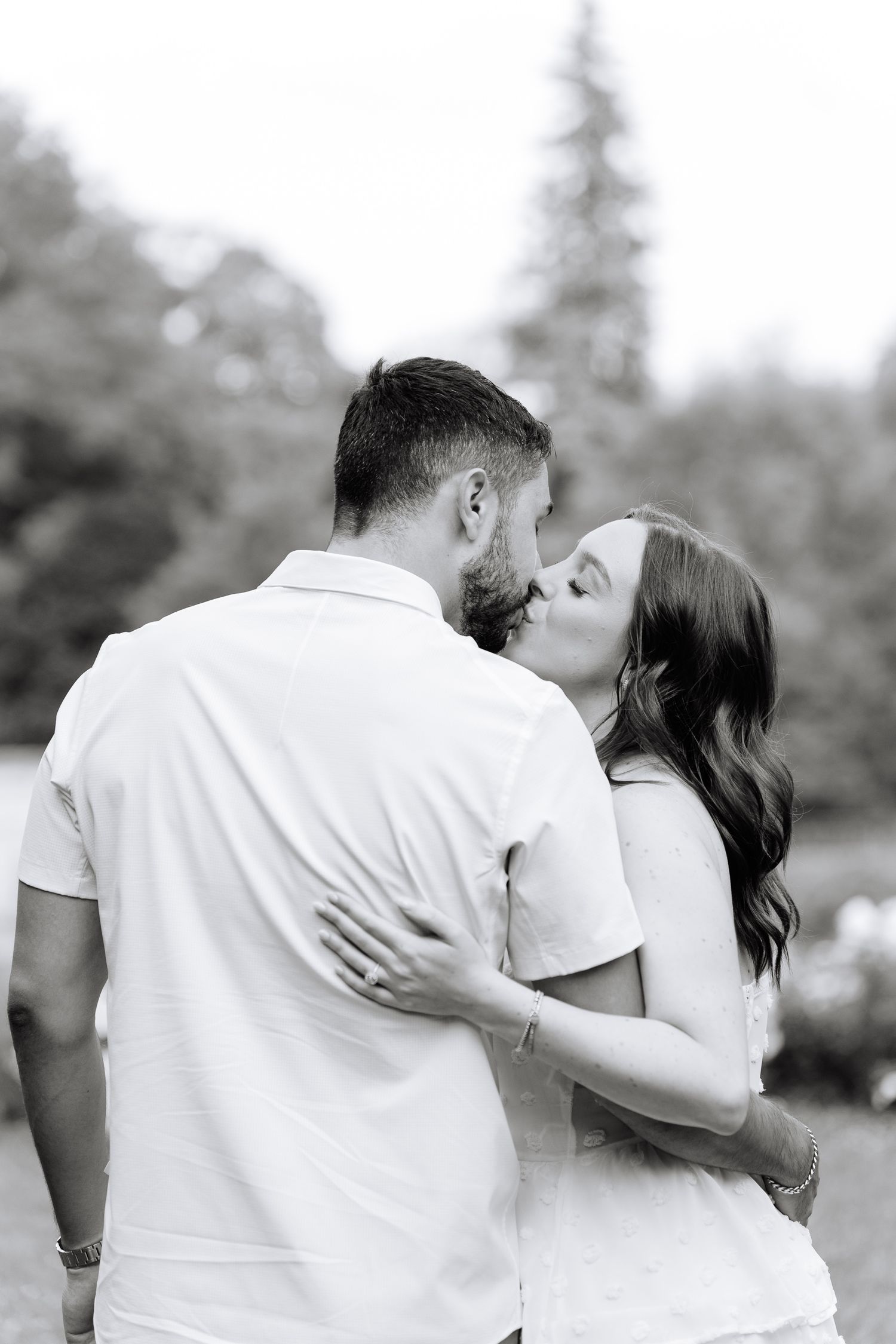 A black and white portrait of a couple sharing an intimate kiss in a garden setting.