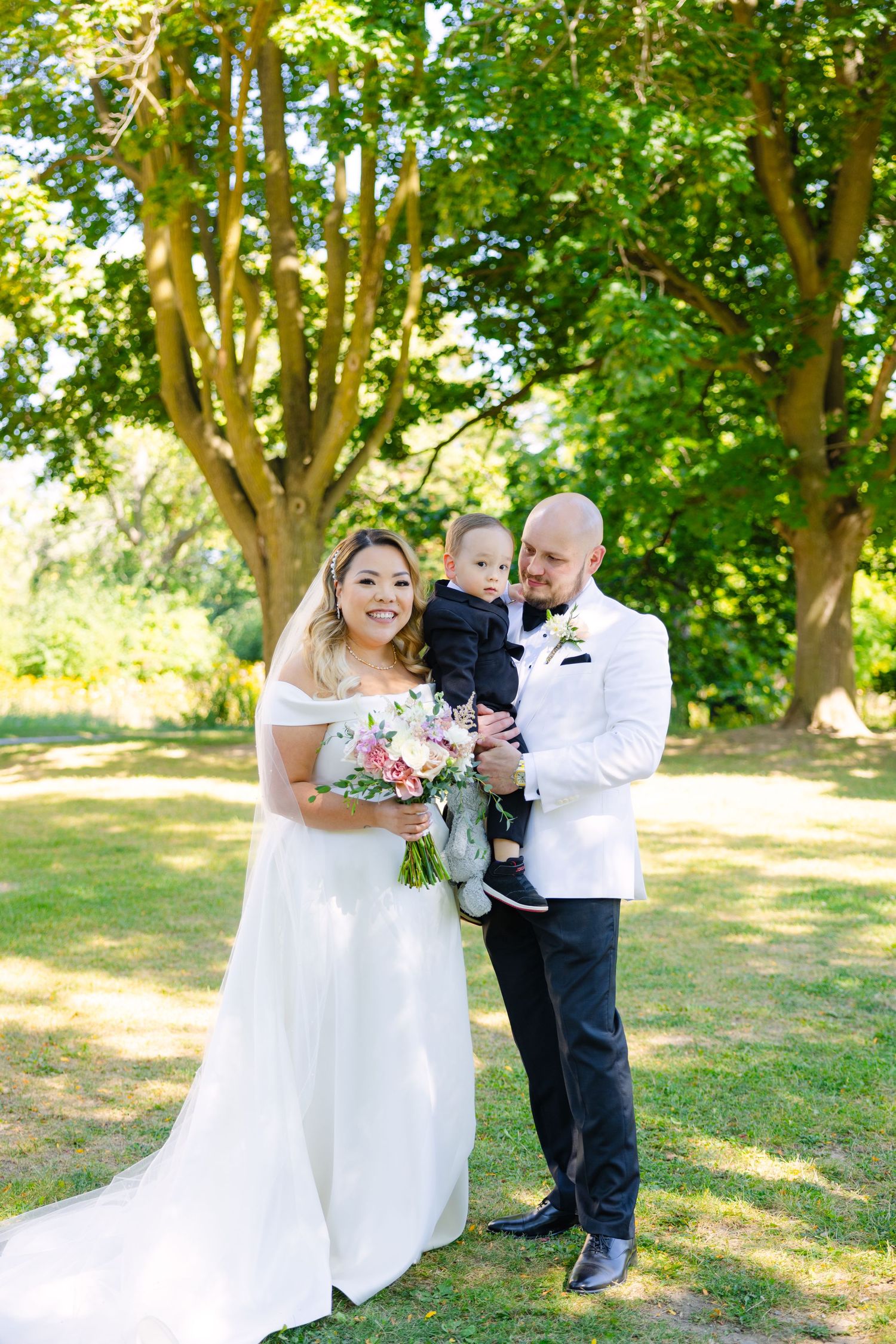 Joyful wedding portrait in sunny garden setting with white formal attire.