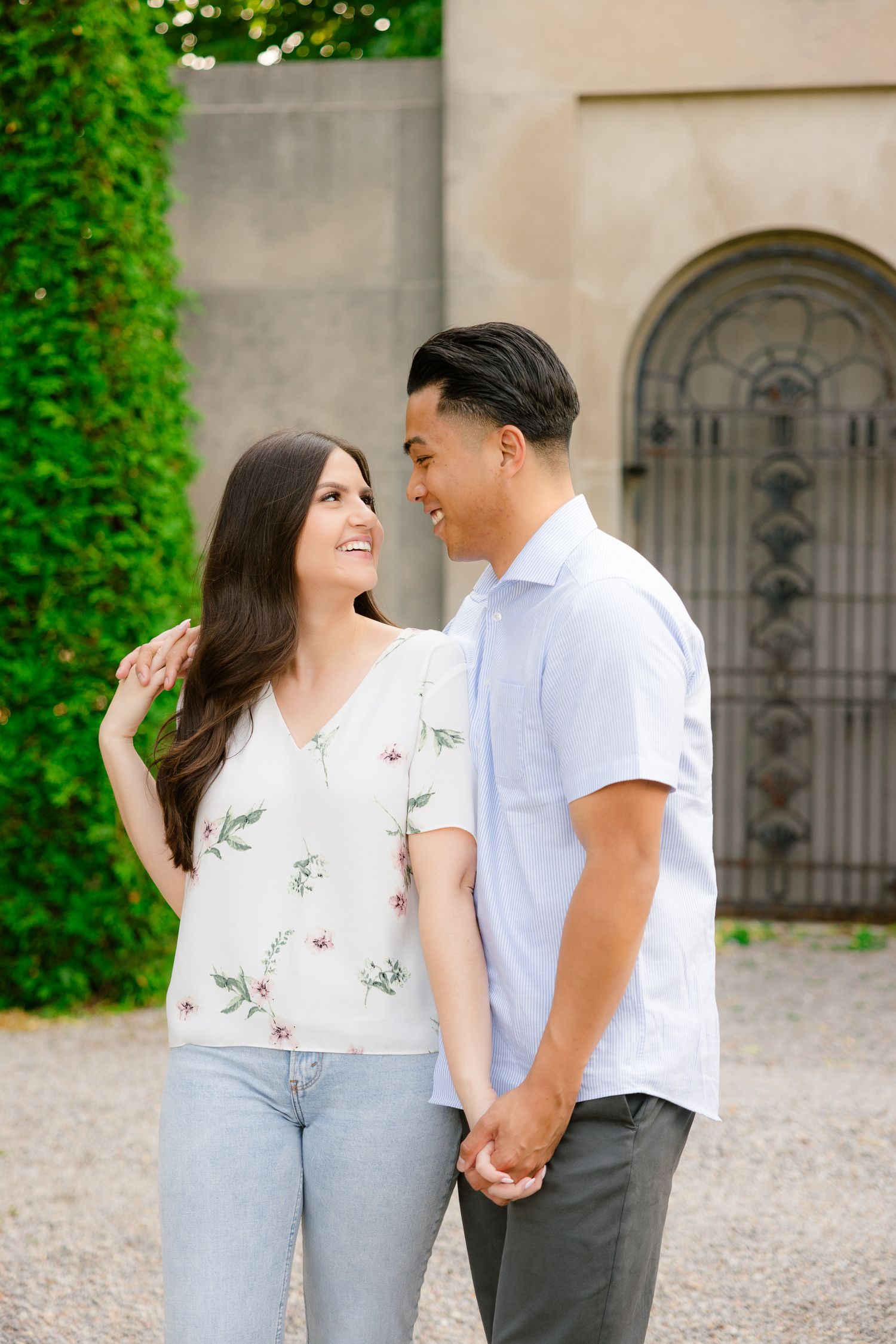 A joyful couple shares a laugh while posing in front of an elegant stone archway and hedges.