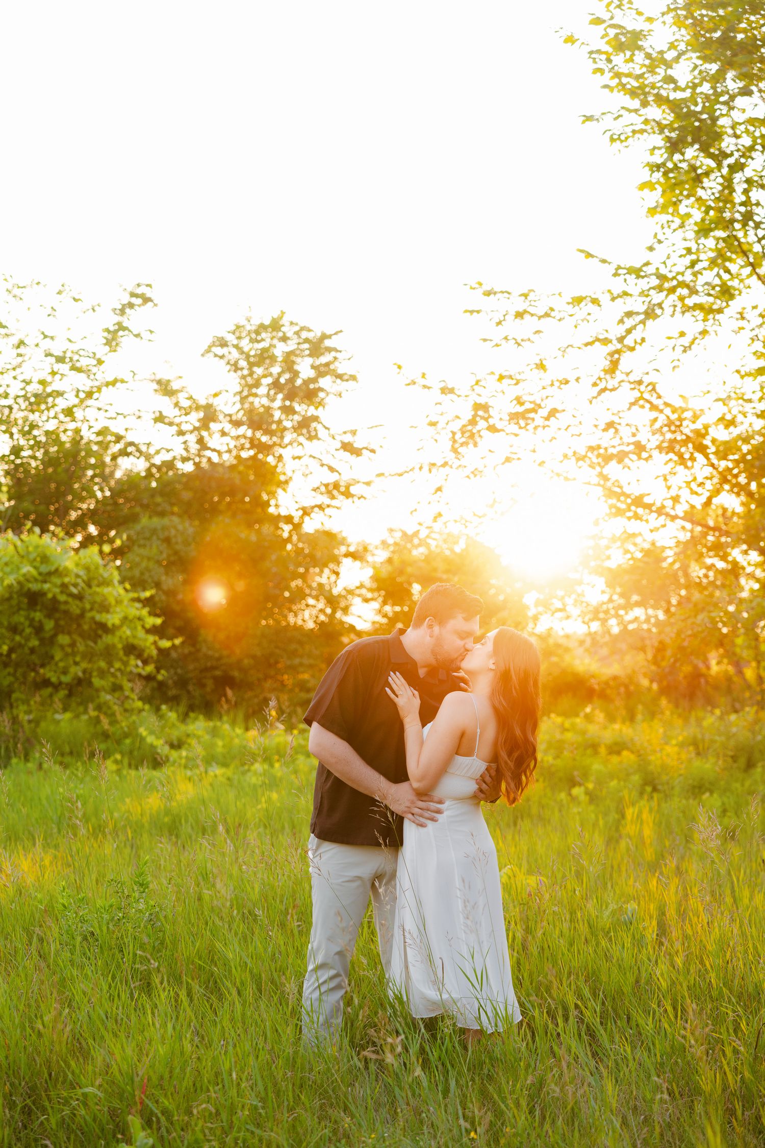 Couple shares tender moment in golden sunlit field during sunset photoshoot.