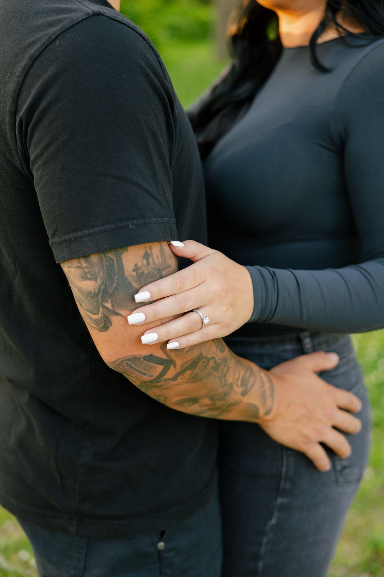 Close-up detail of hands touching tattooed arm in an intimate outdoor portrait.