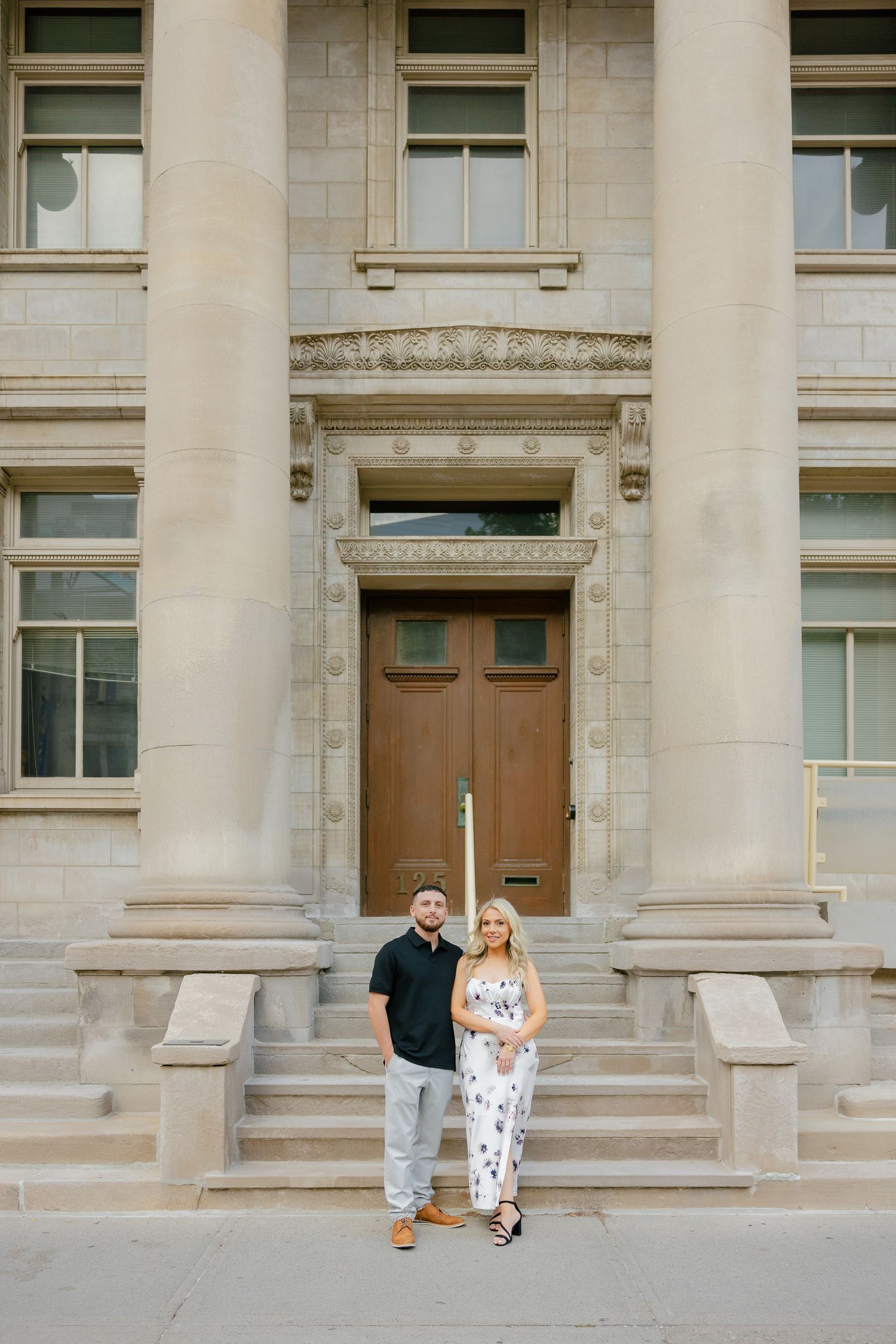 A couple poses formally in front of a historic building entrance with columns.