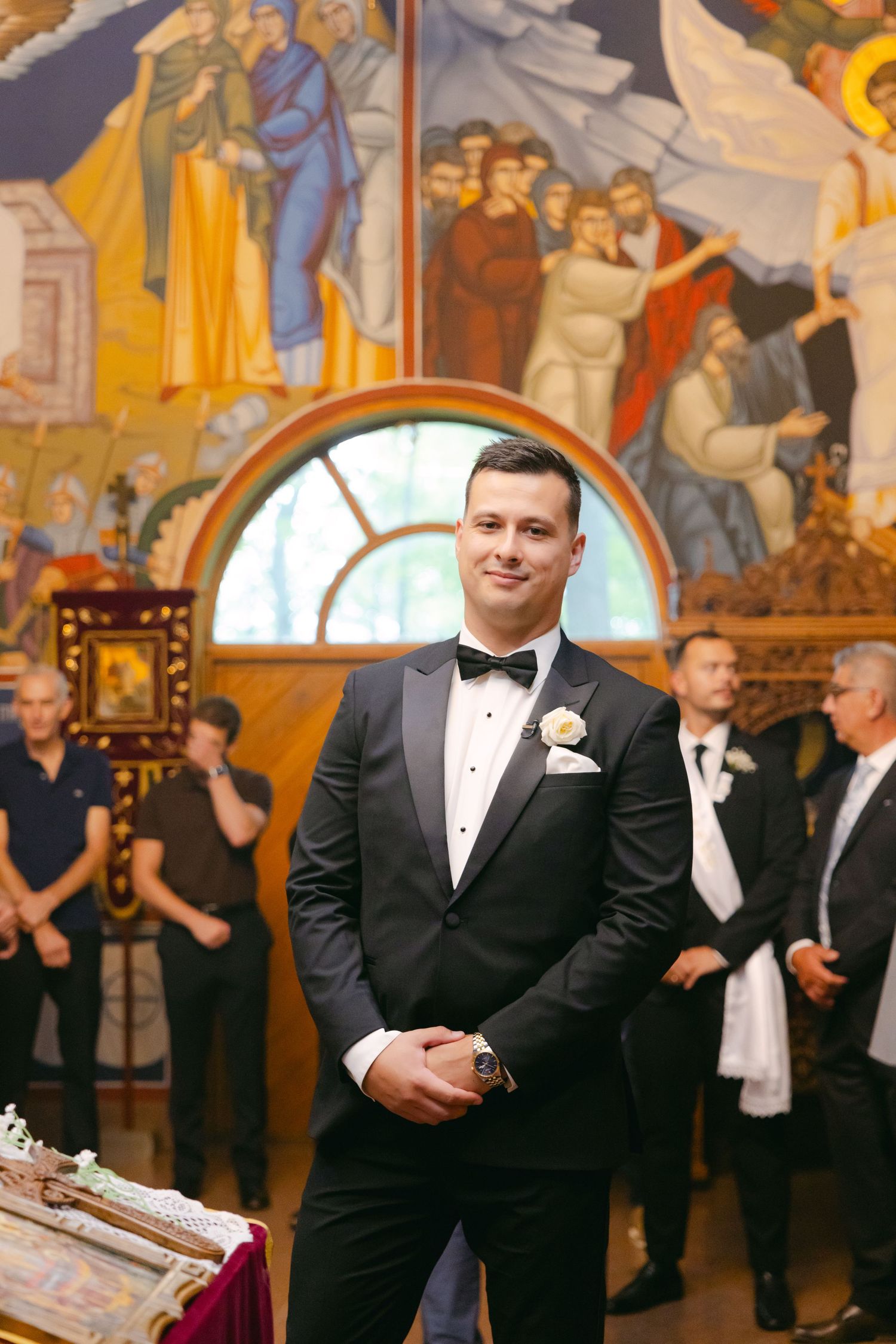 Classic formal attire against backdrop of colorful church murals and arched window.