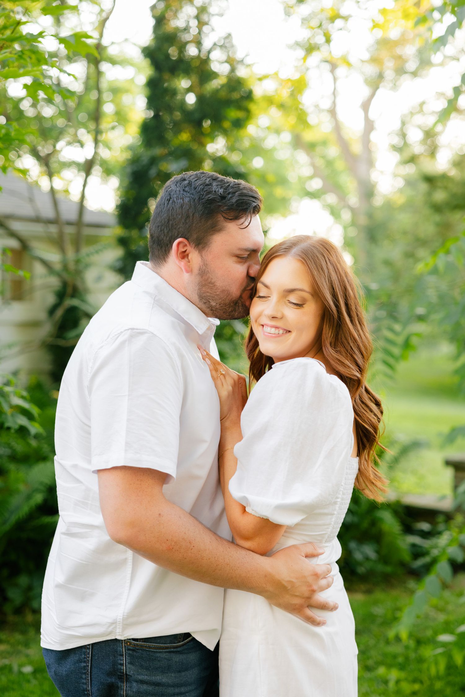 Two people sharing an affectionate moment in a sunlit garden setting wearing coordinating white outfits.