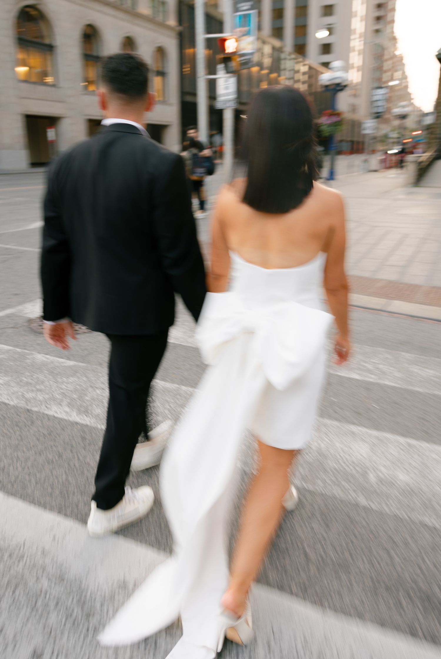 Back view of couple walking down city street in formal wedding attire.