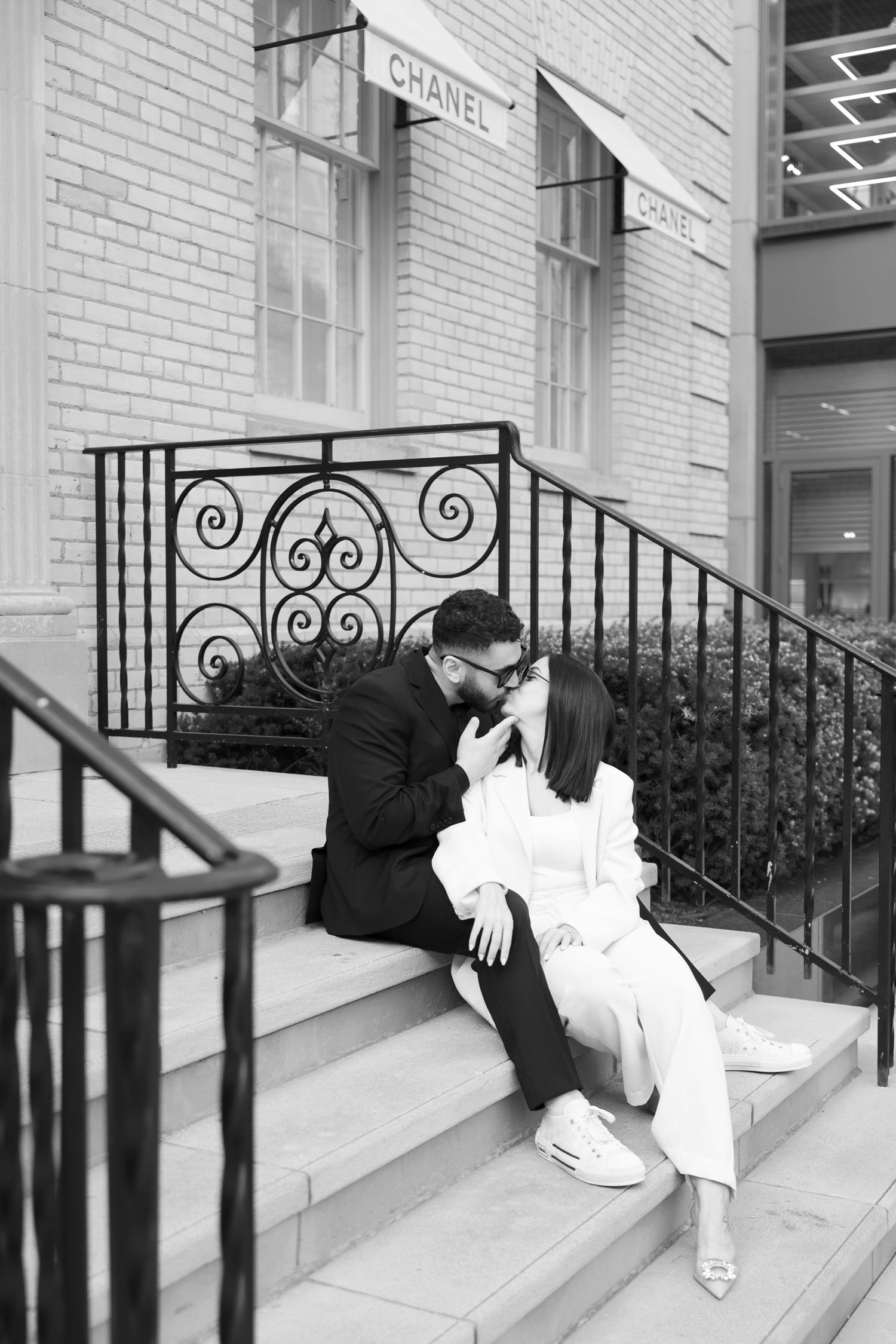 Black and white photo of a couple sitting intimately on steps with ornate iron railings.