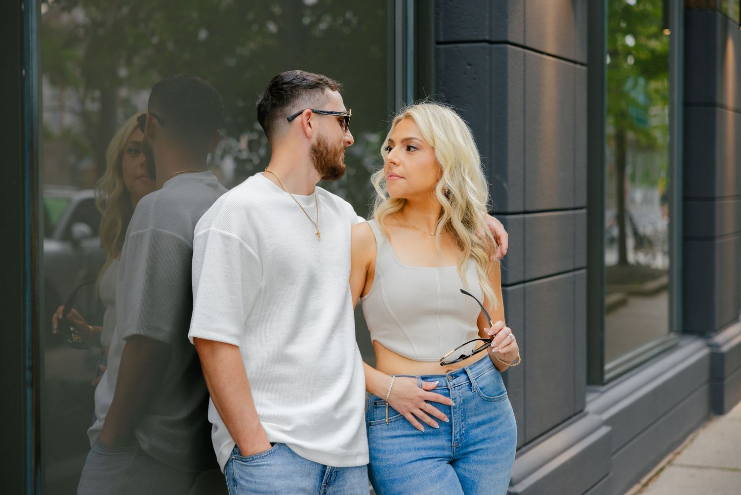 A couple in casual wear sharing an intimate moment against a modern building wall.
