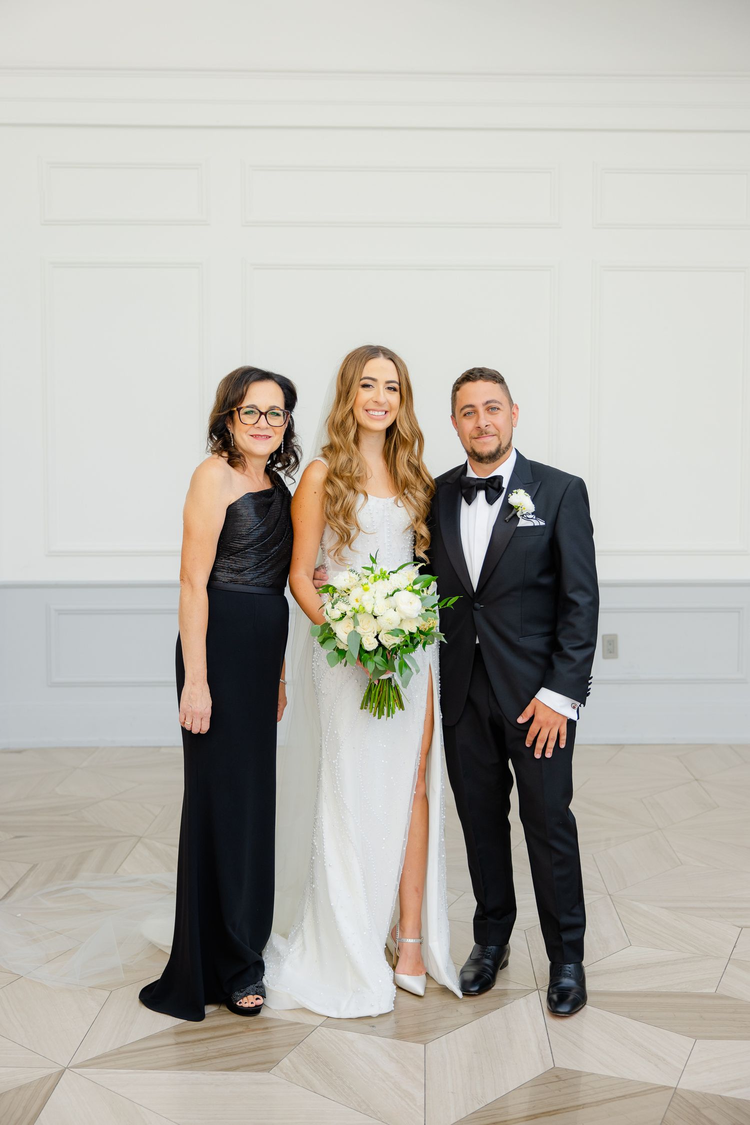 Wedding party portrait of three people in formal attire against light interior backdrop.
