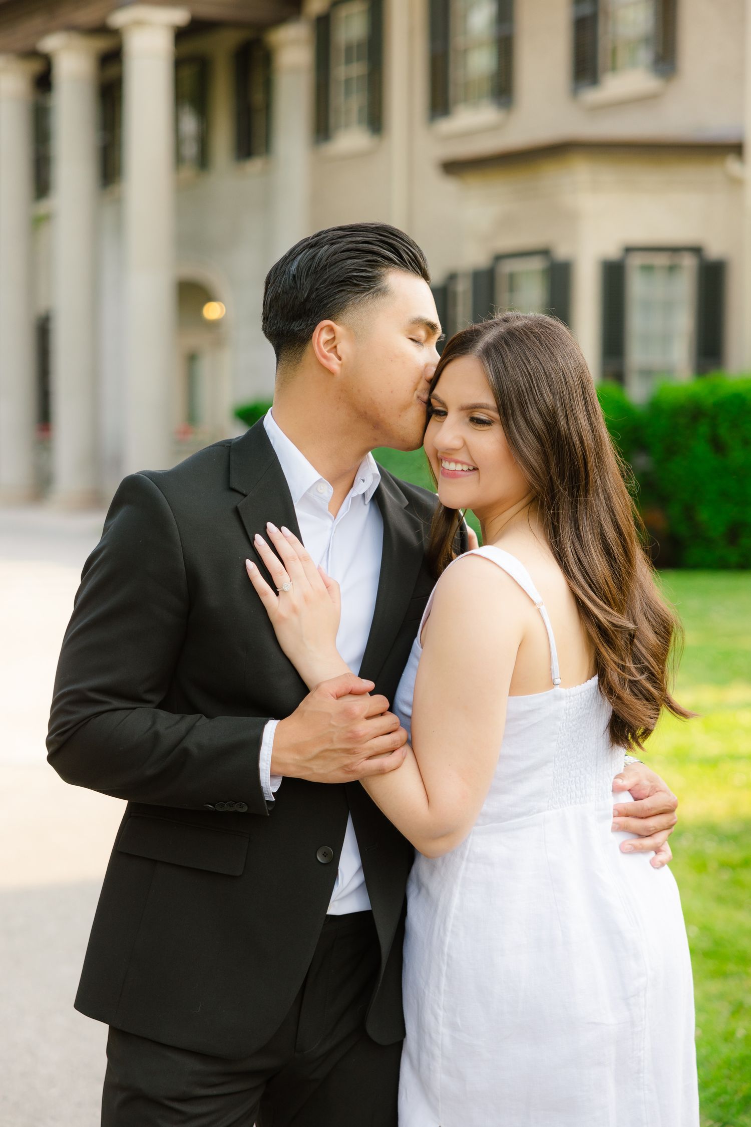 Intimate moment captured between couple in black and white formal wear by grand colonial building.