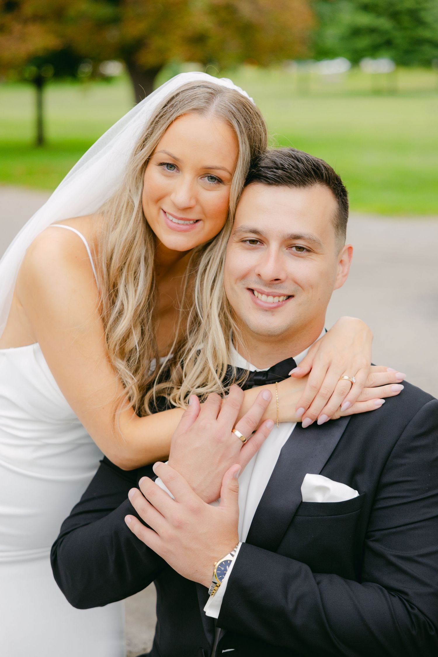 Joyful wedding portrait of couple embracing outdoors with bride in white dress and groom in tuxedo.