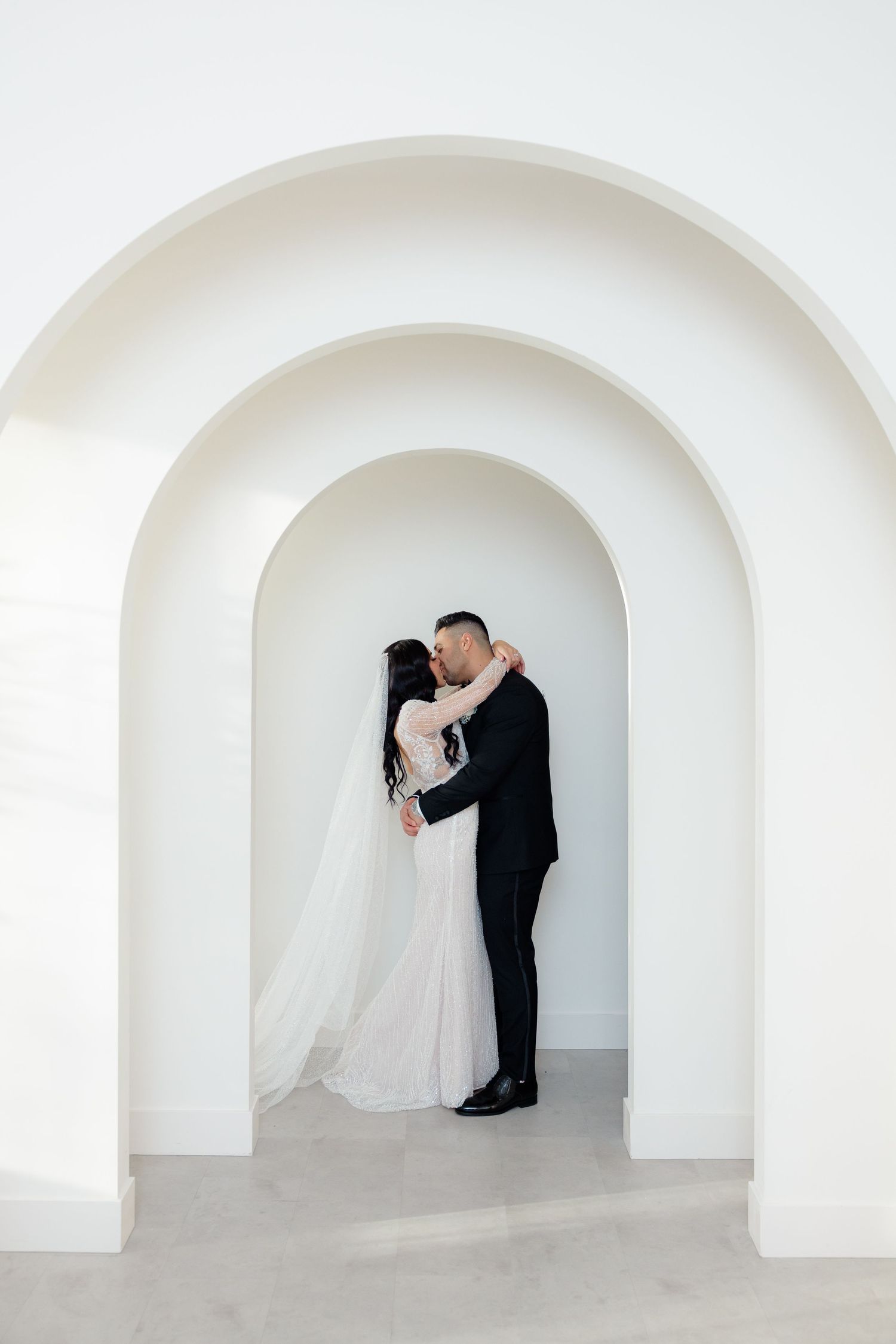 Minimalist wedding photo with couple embracing in white arched hallway.