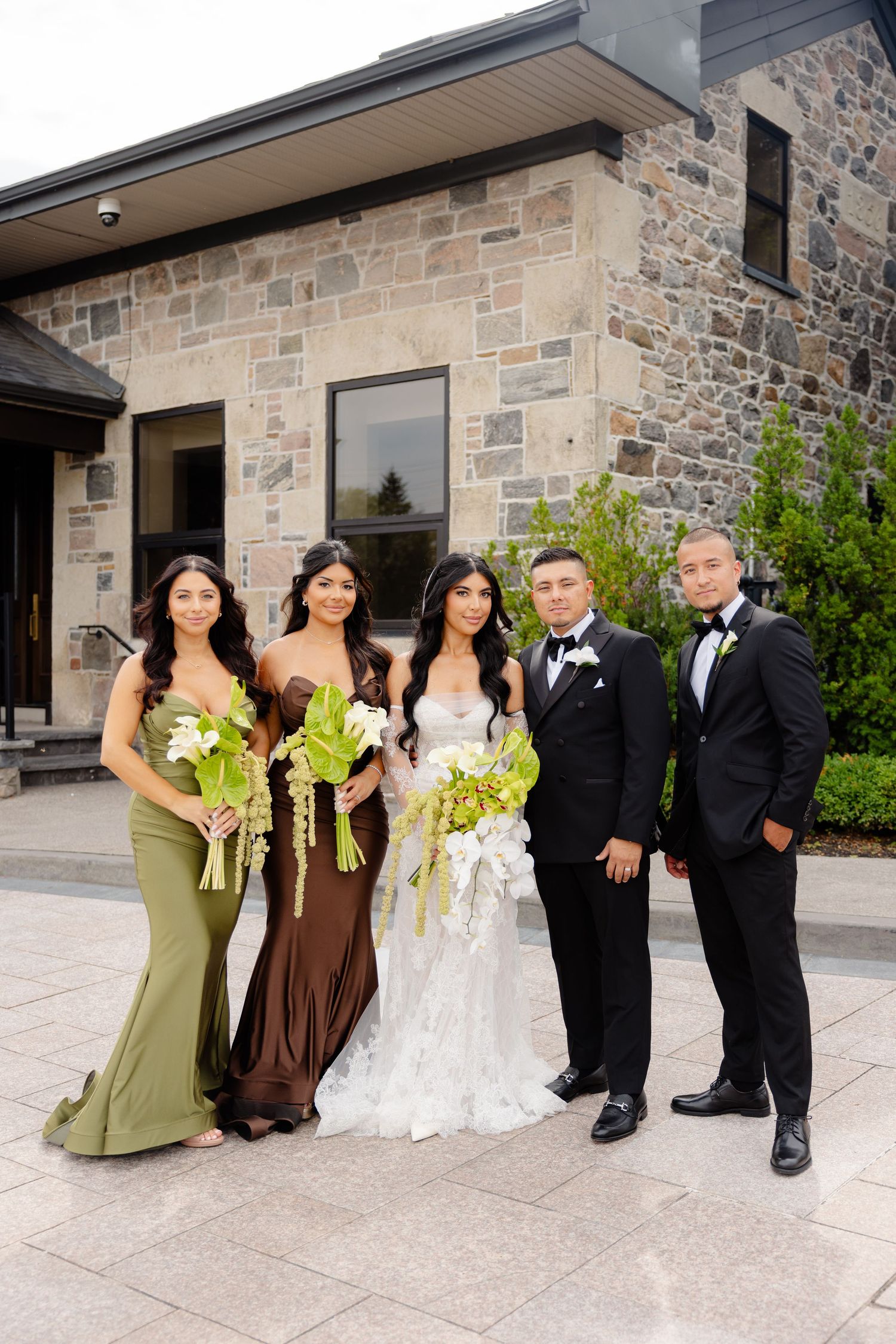 Wedding party poses in sequence against stone building exterior with bridesmaids in brown and green dresses.