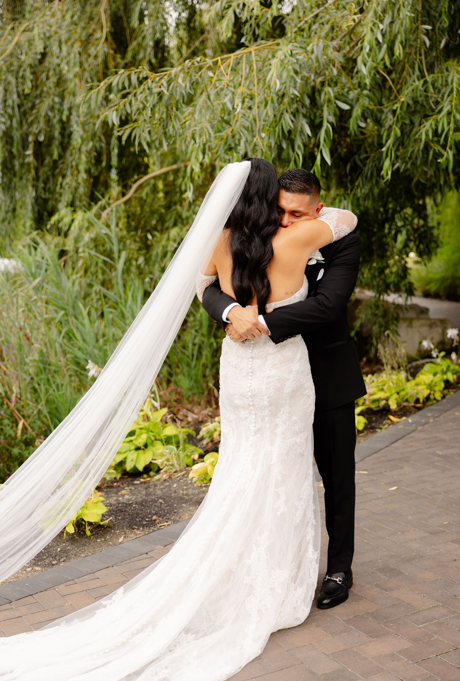 A romantic moment between newlyweds under a weeping willow tree with a flowing white wedding dress and cathedral veil.