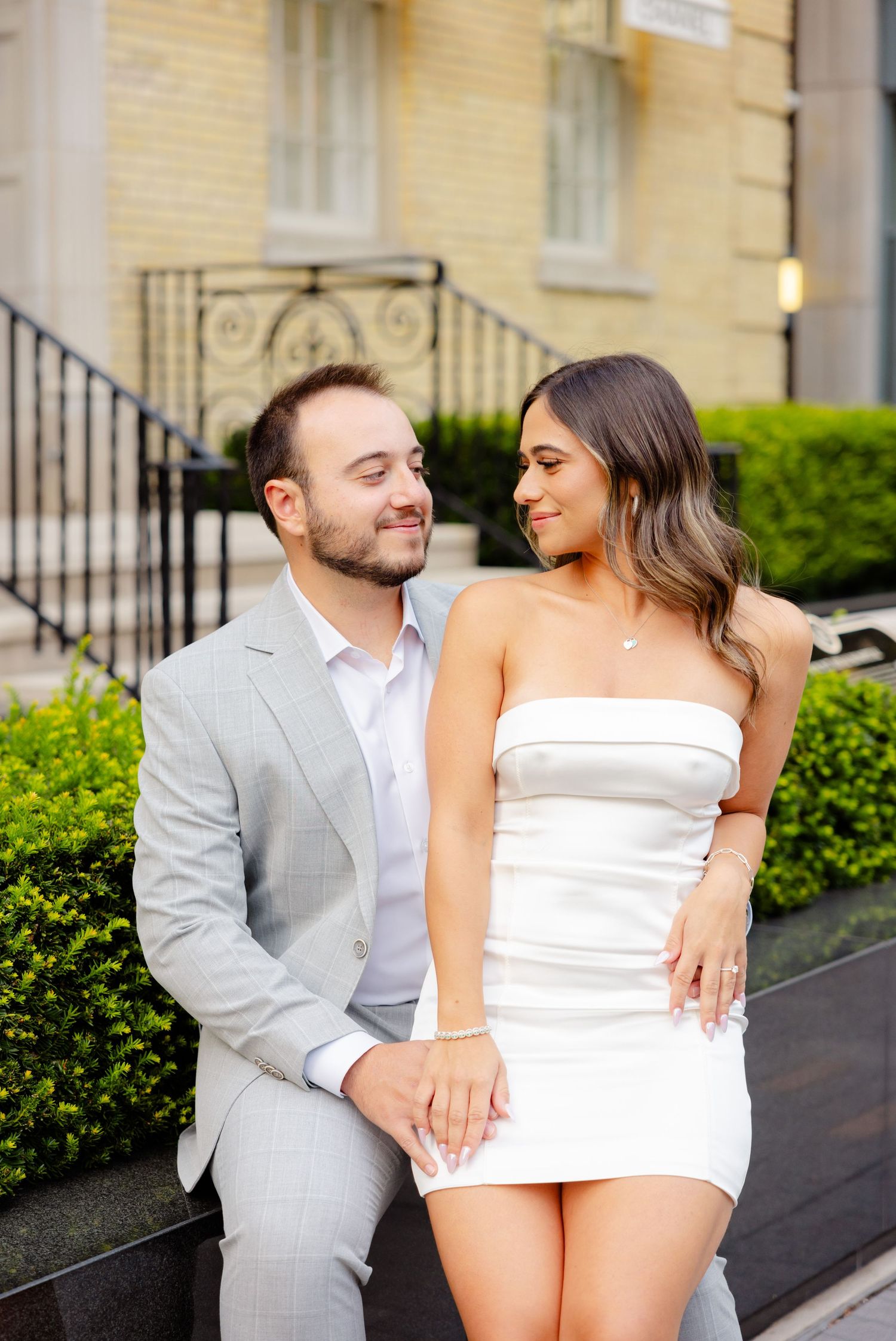 Happy couple shares intimate moment while seated outside Chanel store in formal attire.