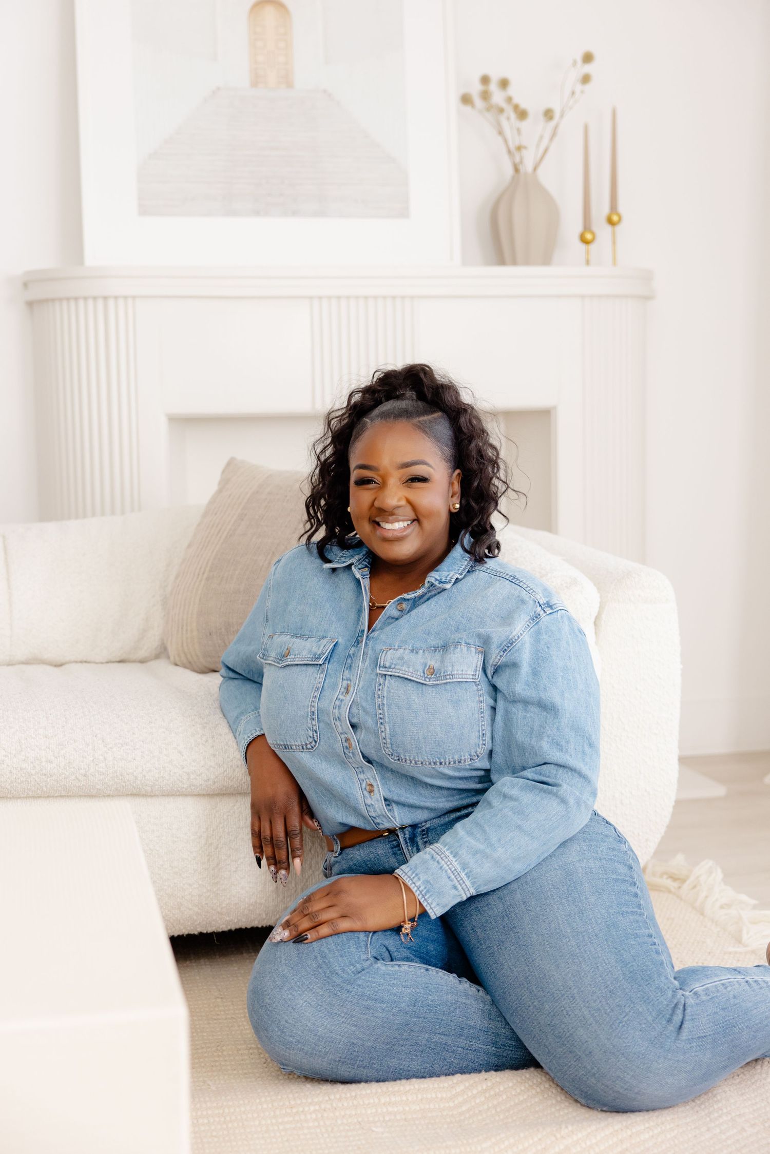 A woman wearing double denim lounges comfortably on a white couch in a bright minimalist living room setting.