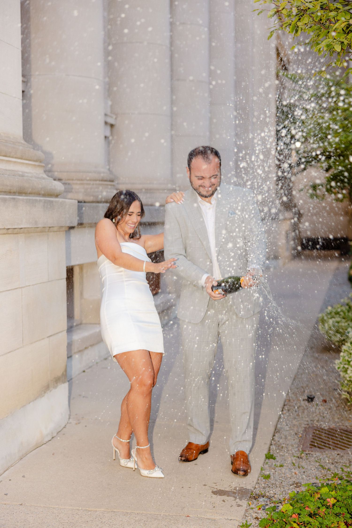 Celebratory moment with champagne spray against stone column backdrop.
