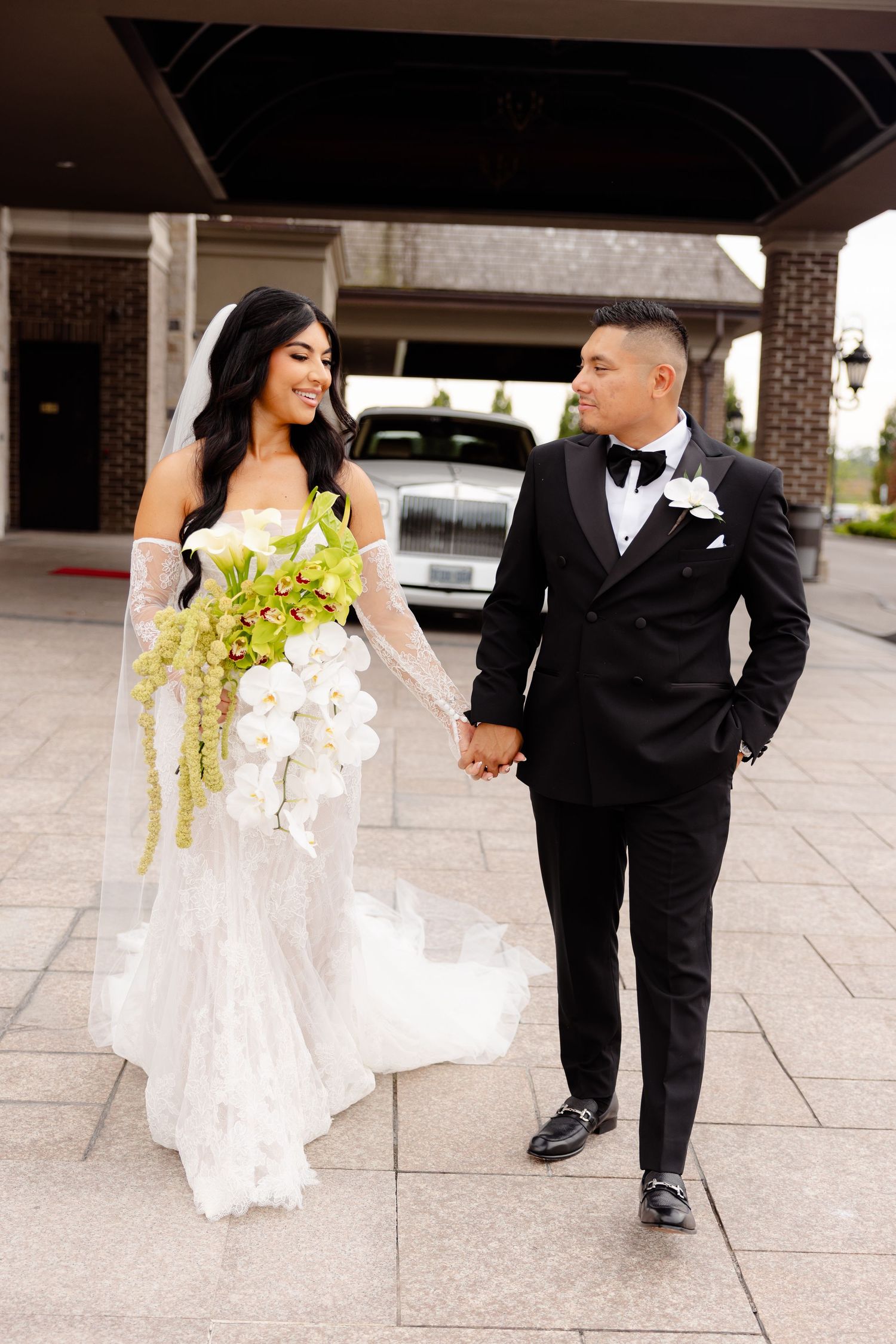 Black and white themed wedding photo showing bride in flowing dress and groom in classic tuxedo walking together.