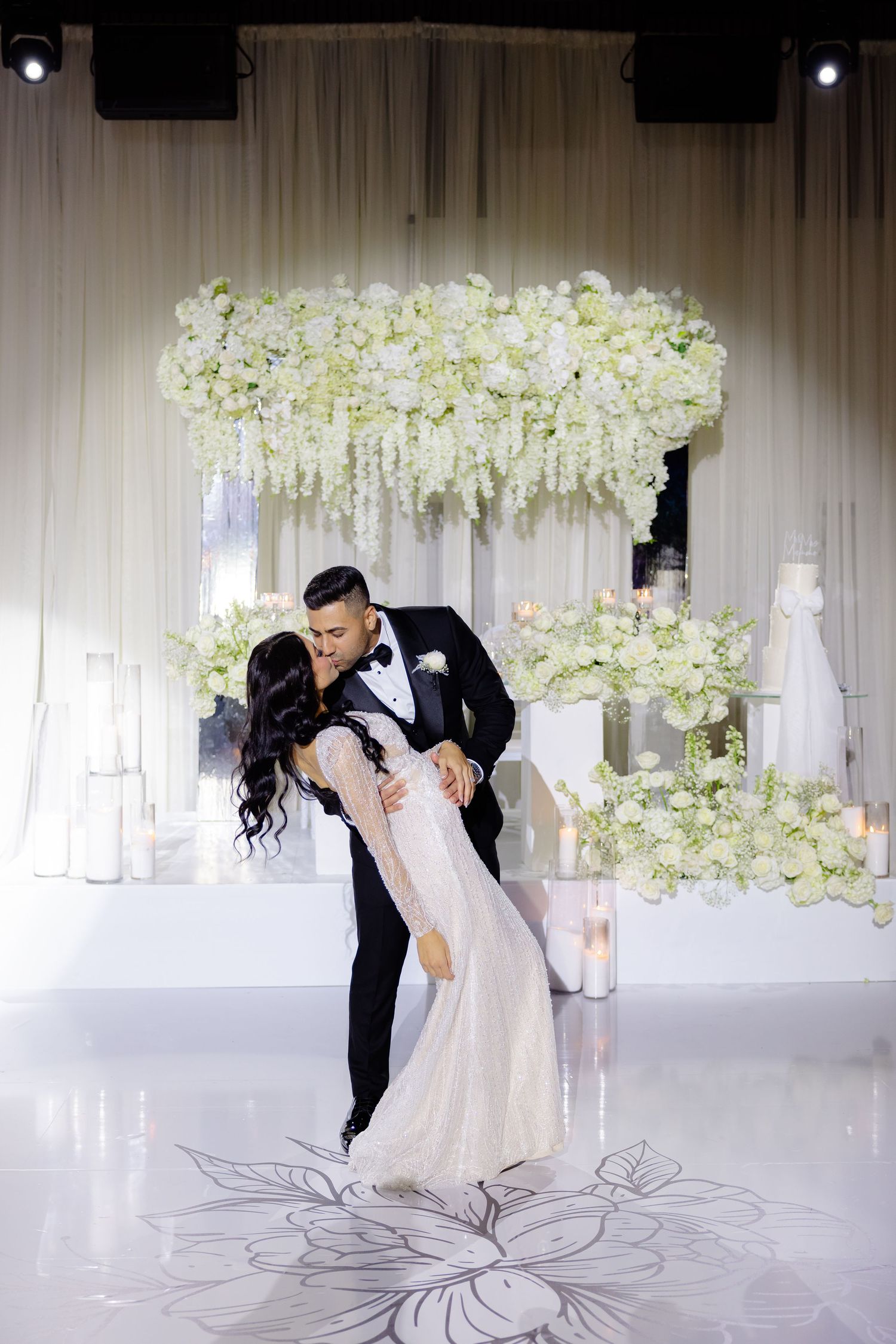 Romantic wedding dance pose beneath a luxurious white floral arch installation.