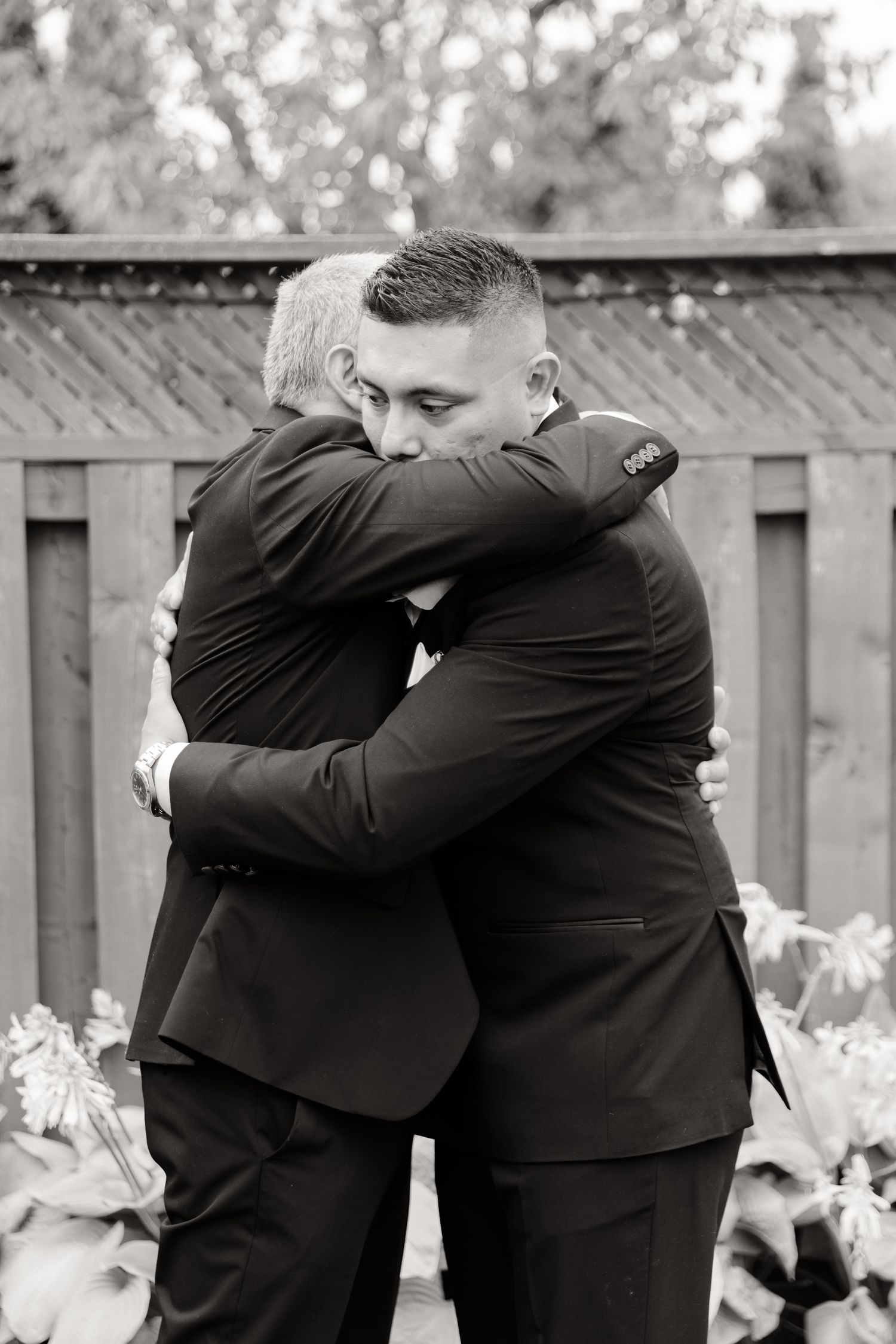 Four black and white images show people in dark suits sharing emotional embraces outdoors.