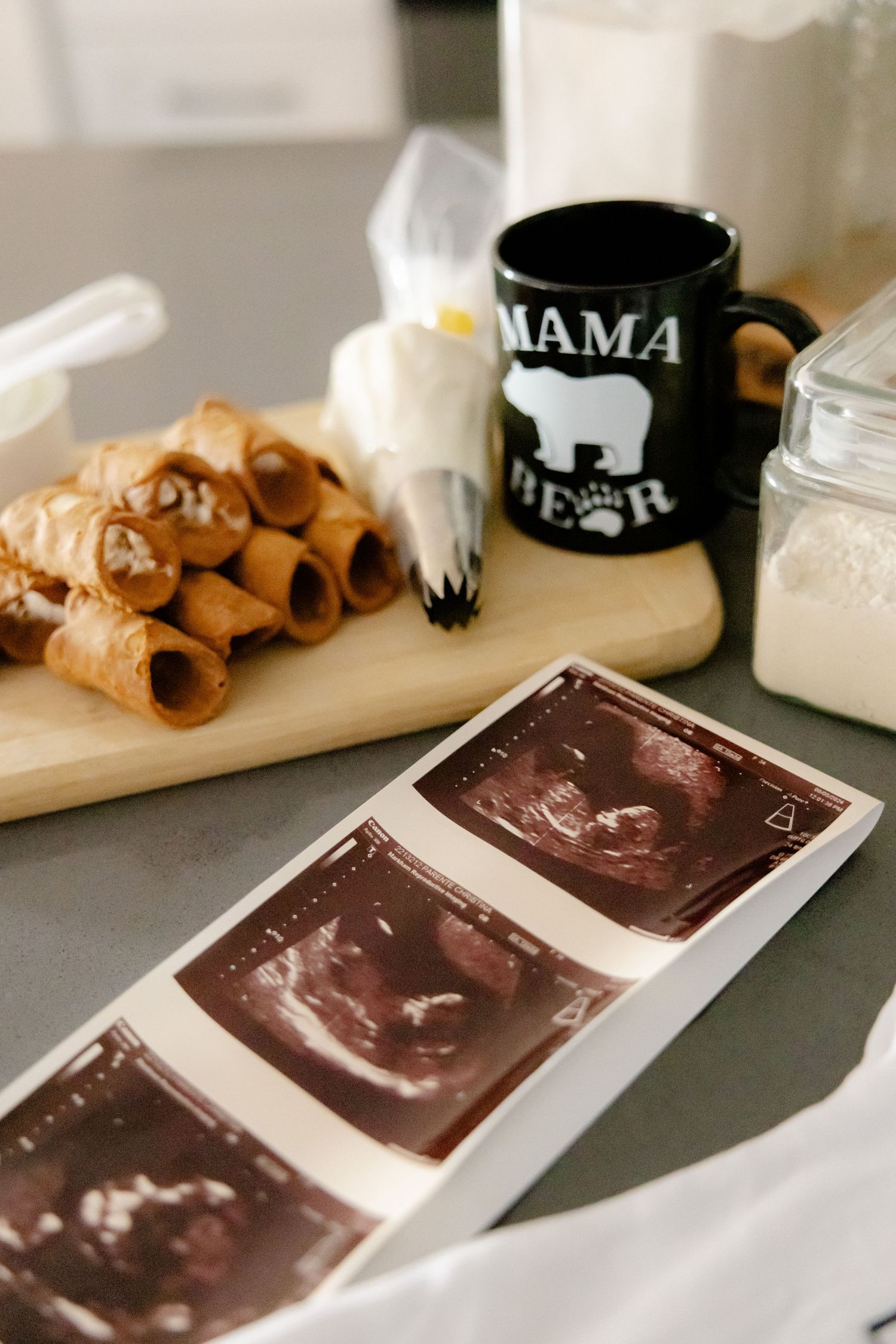 A table setting with ultrasound images, pastries, and a mug labeled 'MAMA BEAR' for a pregnancy announcement.