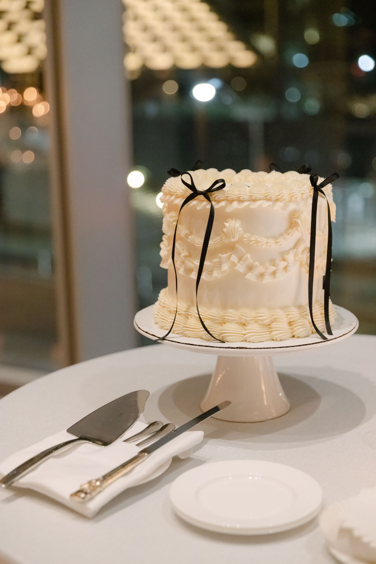 White wedding cake with delicate piping details and black ribbon accents on a white cake stand.