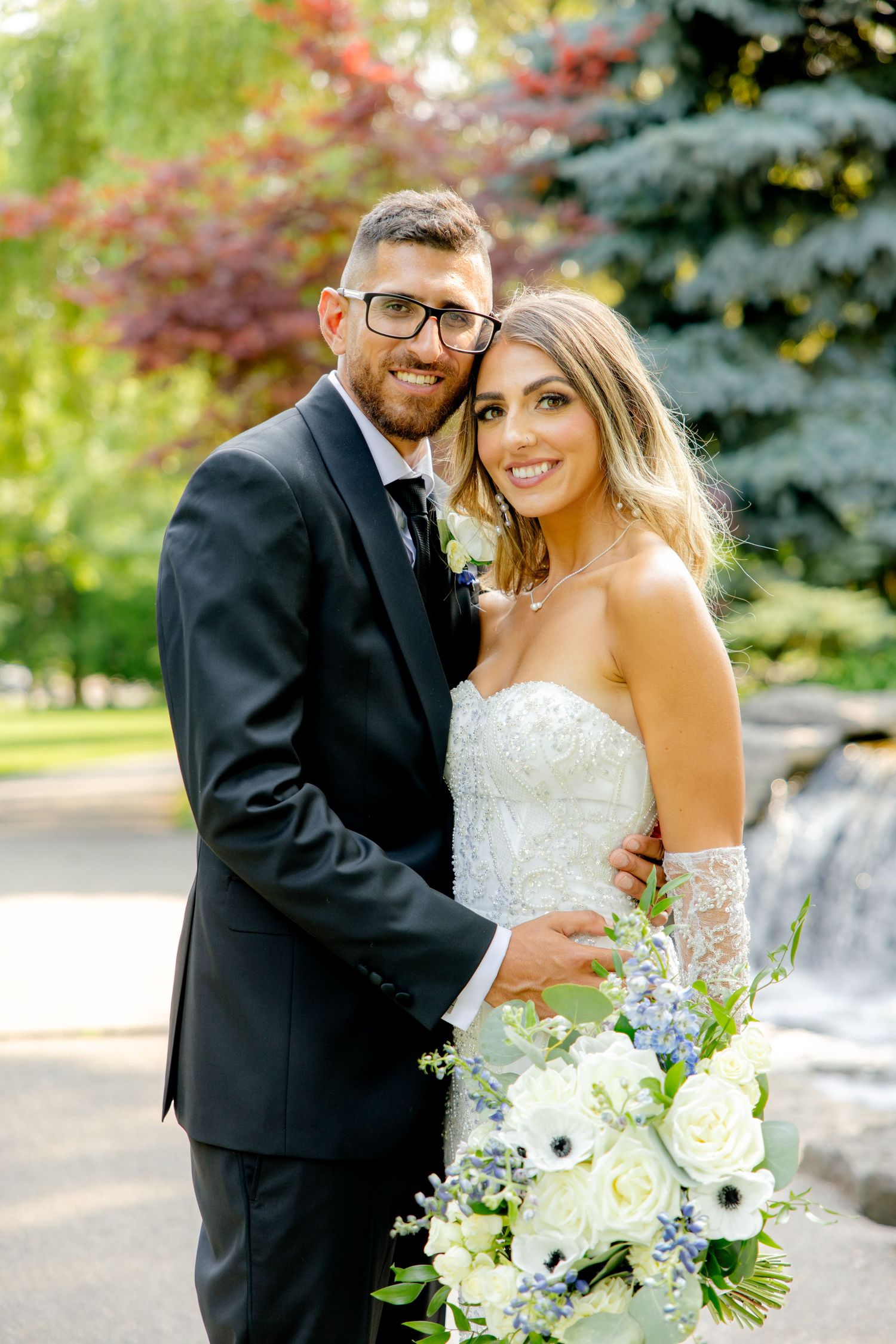A couple shares an intimate moment while posing for wedding photos in front of a garden waterfall.