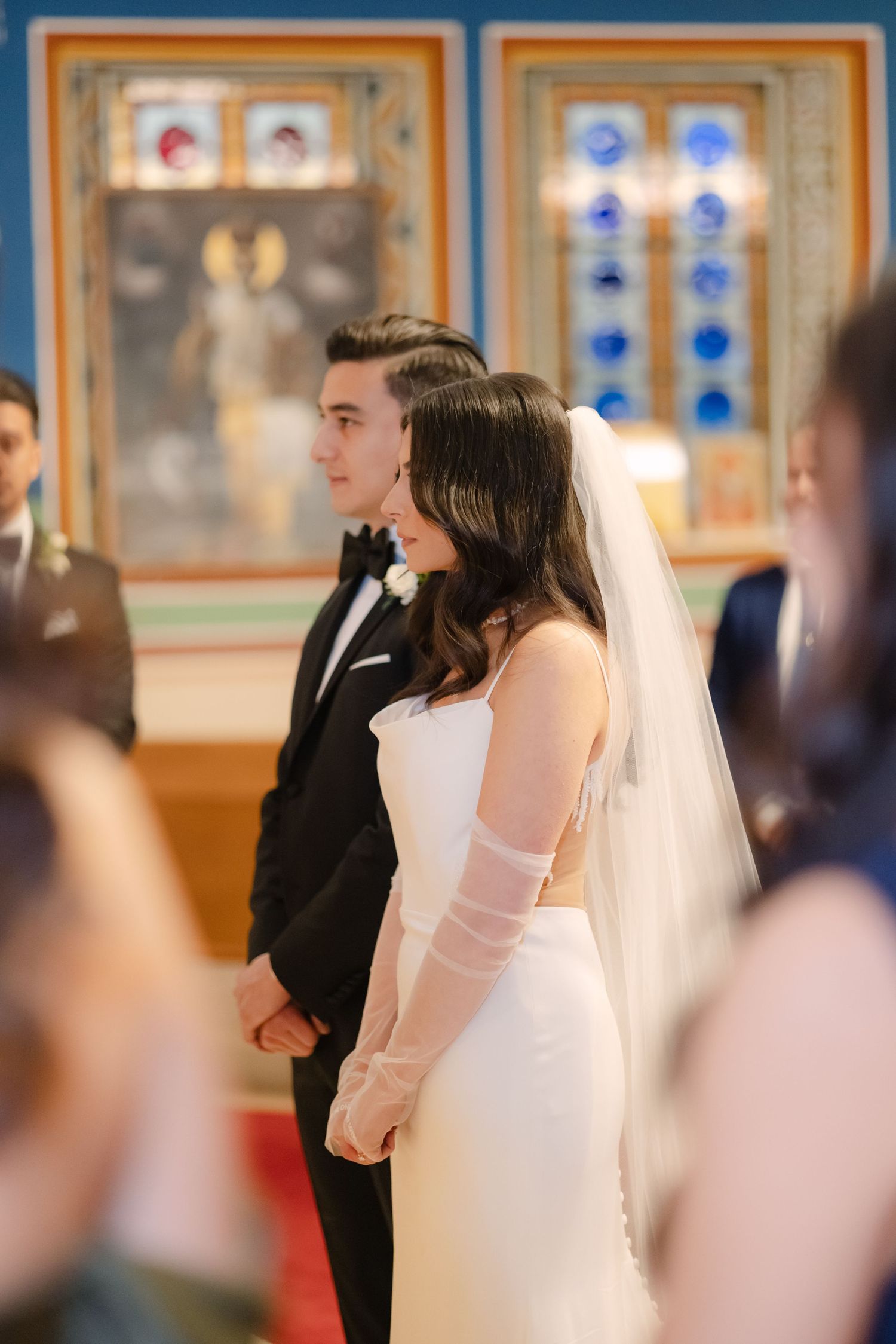 Wedding couple standing at the altar in an orthodox church with stained glass windows.