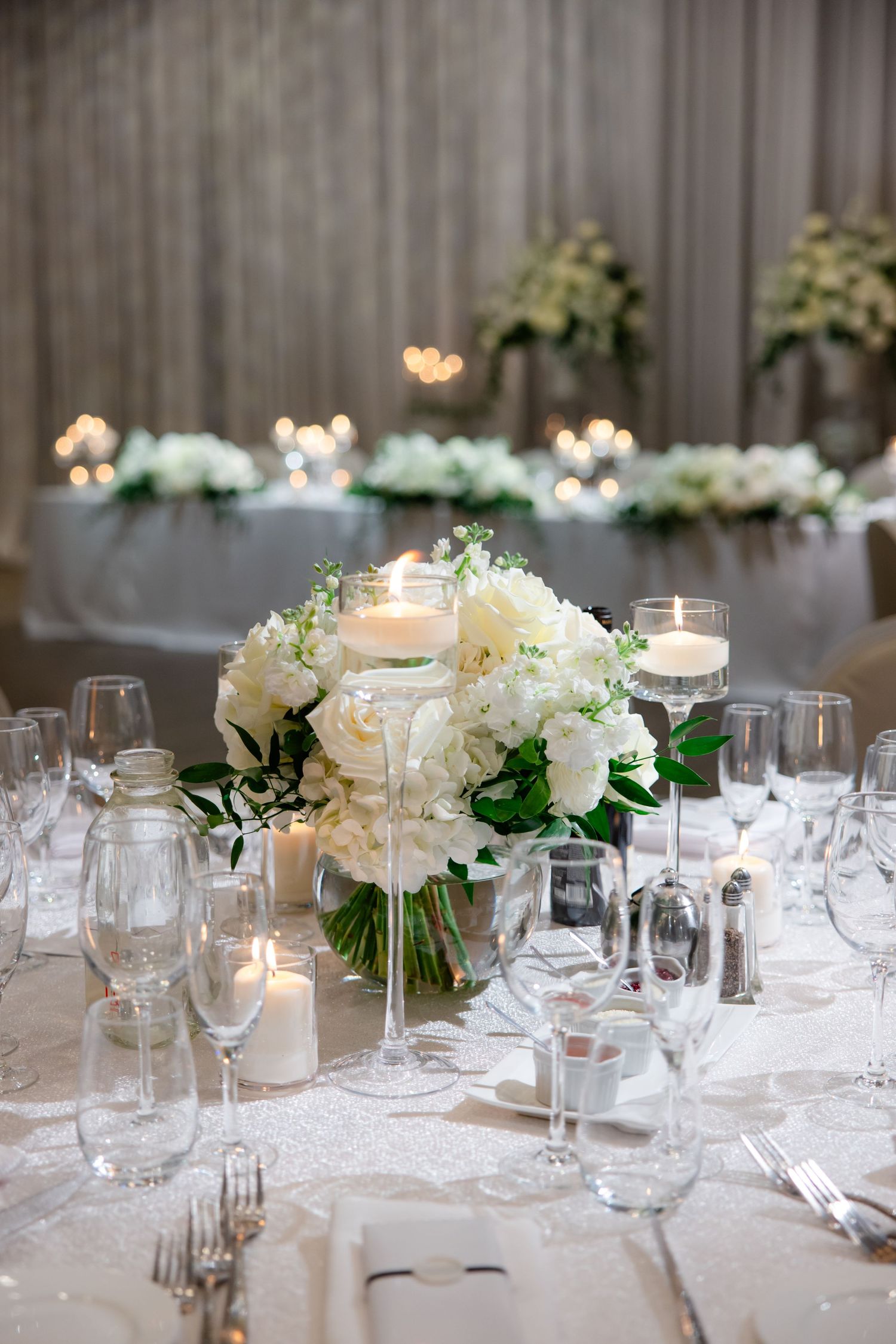 Romantic wedding reception table with white floral centerpiece and glowing votives.