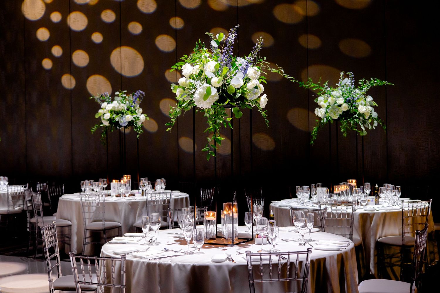 Wedding reception tables decorated with elevated floral arrangements and mood lighting.