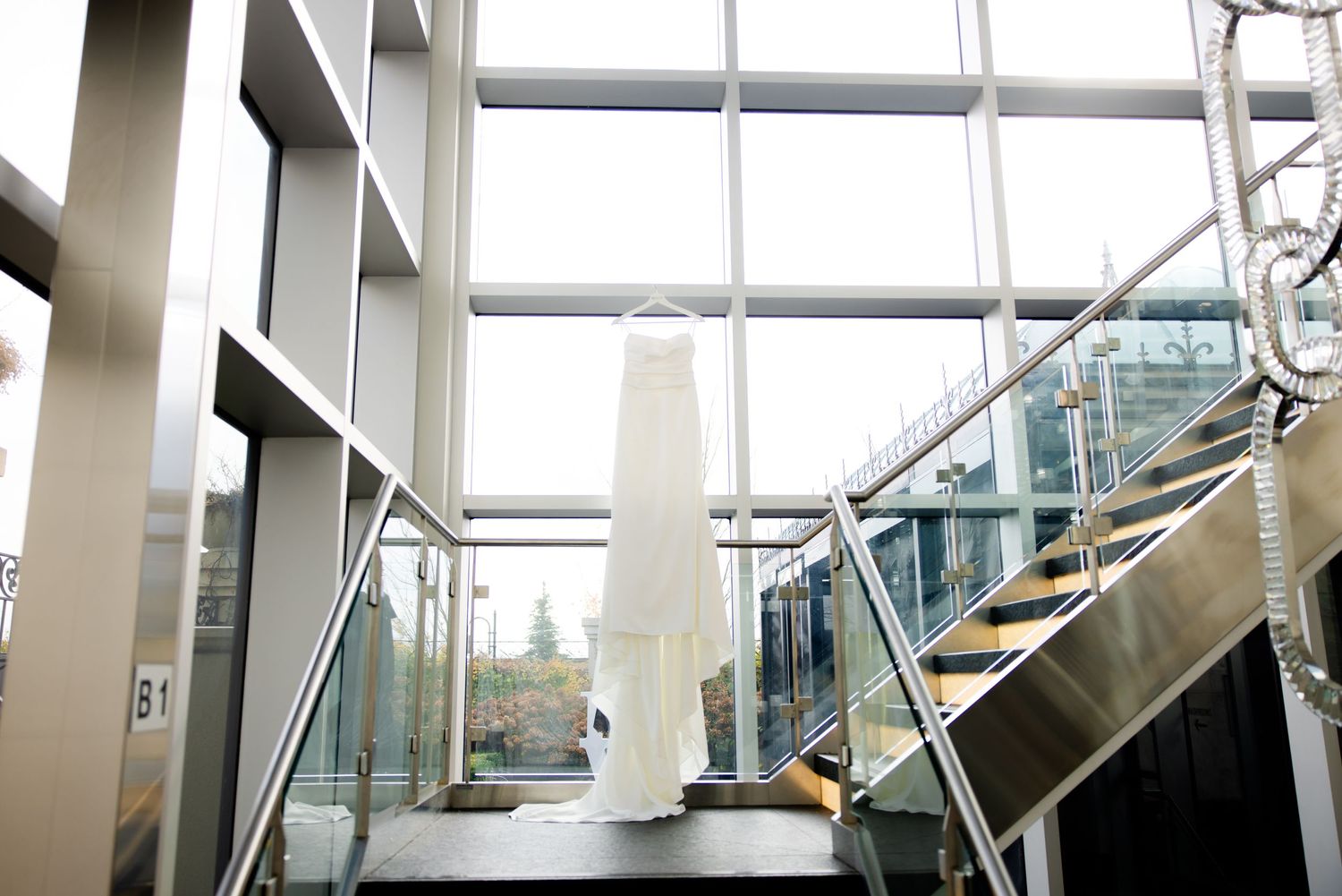 Wedding dress hanging in architectural stairwell with glass and metal details.
