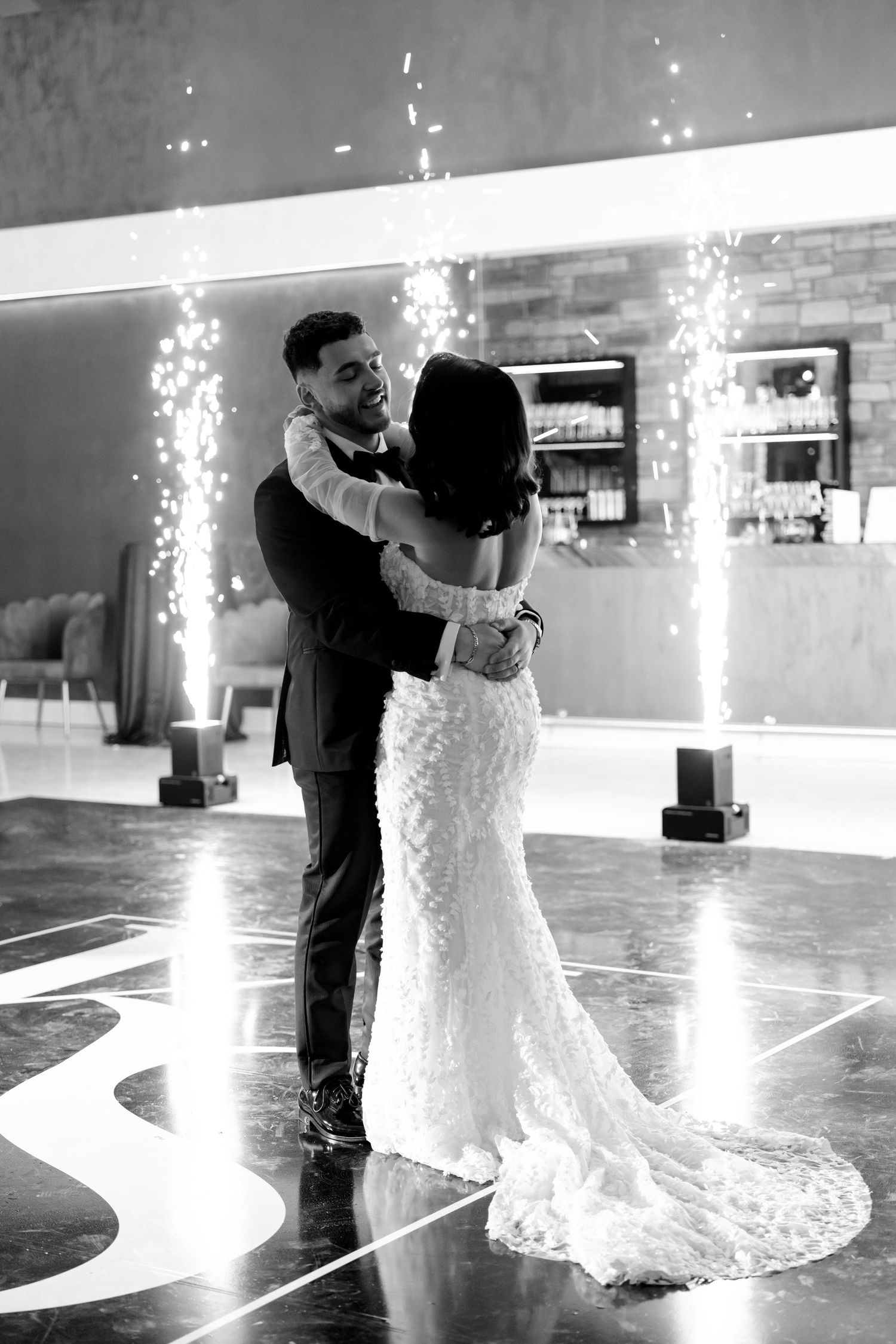 Black and white photo captures a tender first dance moment with sparklers glowing in the background.