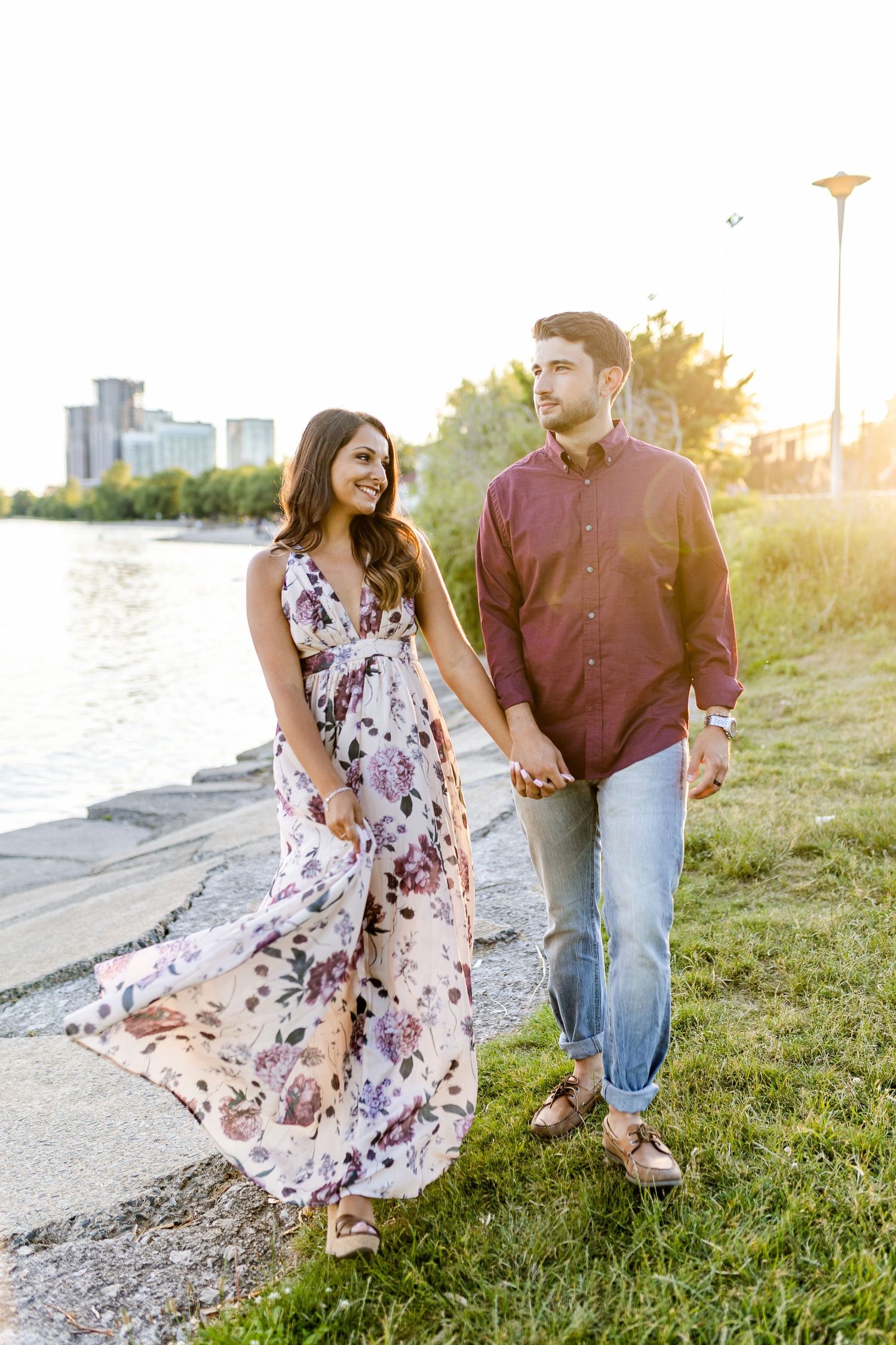 Couple strolling hand in hand on grassy waterfront path during golden hour.