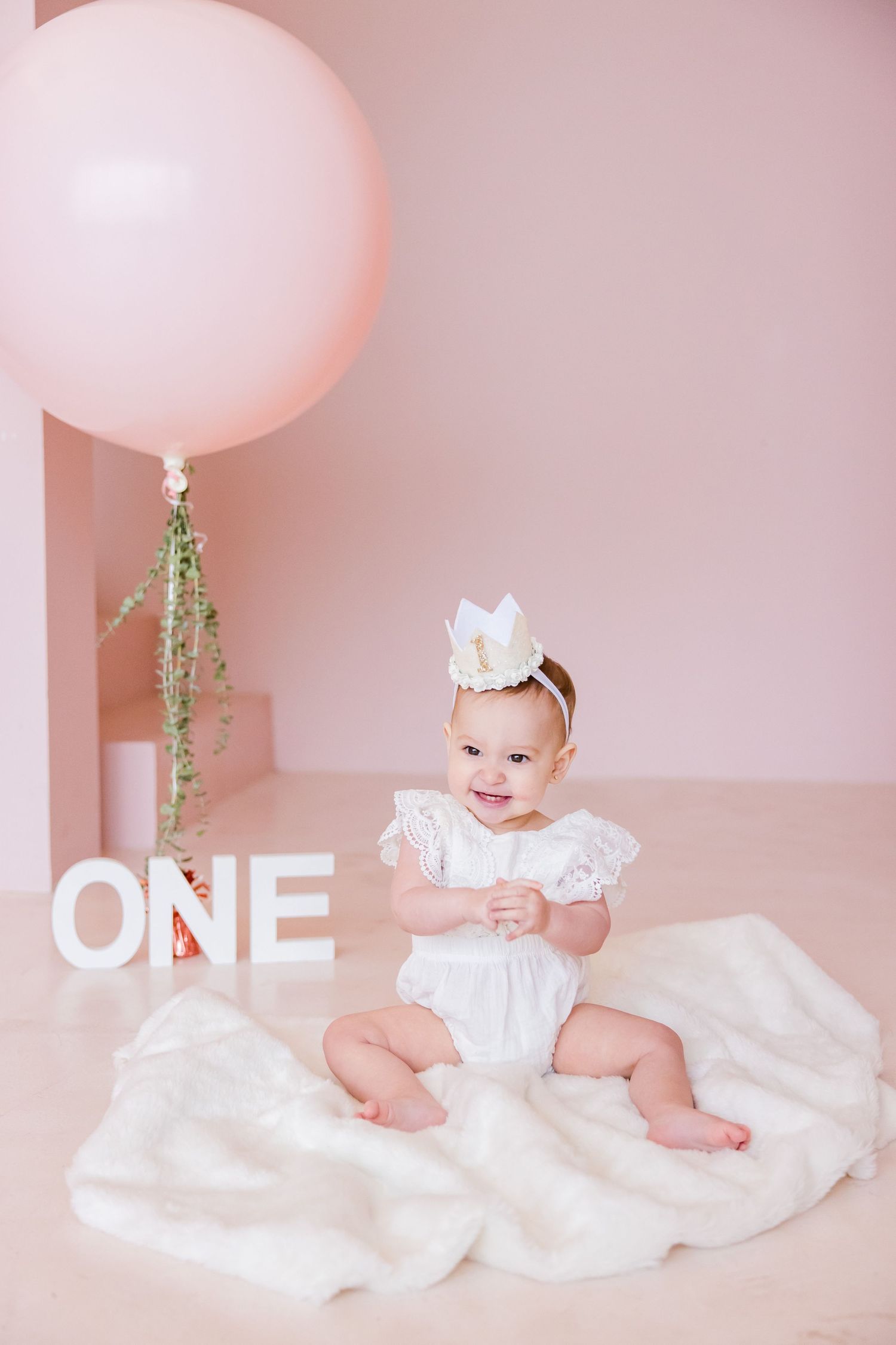 First birthday portrait with large pink balloon and 'ONE' text against pink wall.