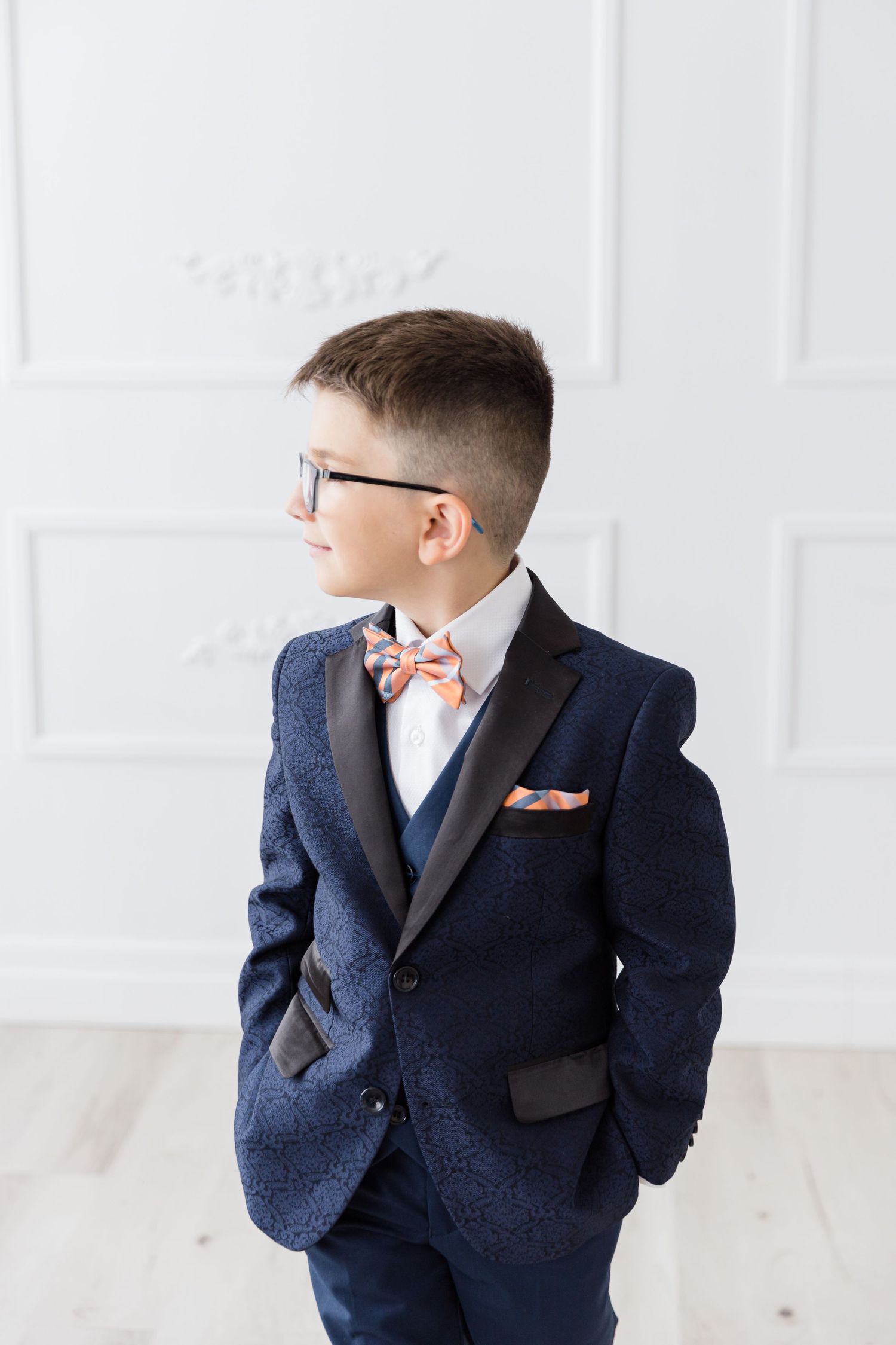 Side profile of youth in formal attire against white paneled wall.