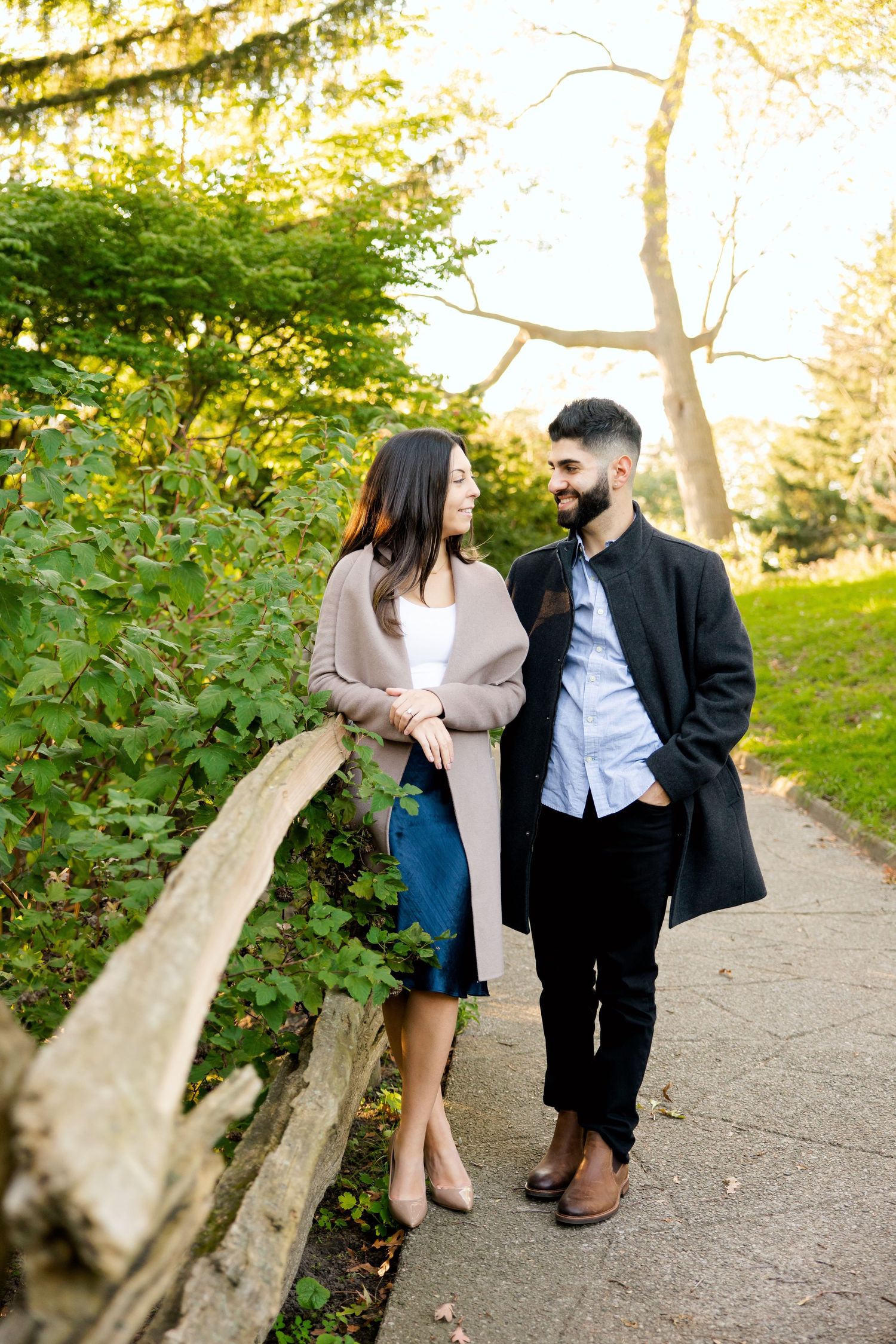 Couple in stylish coats walking together on park path during golden hour.