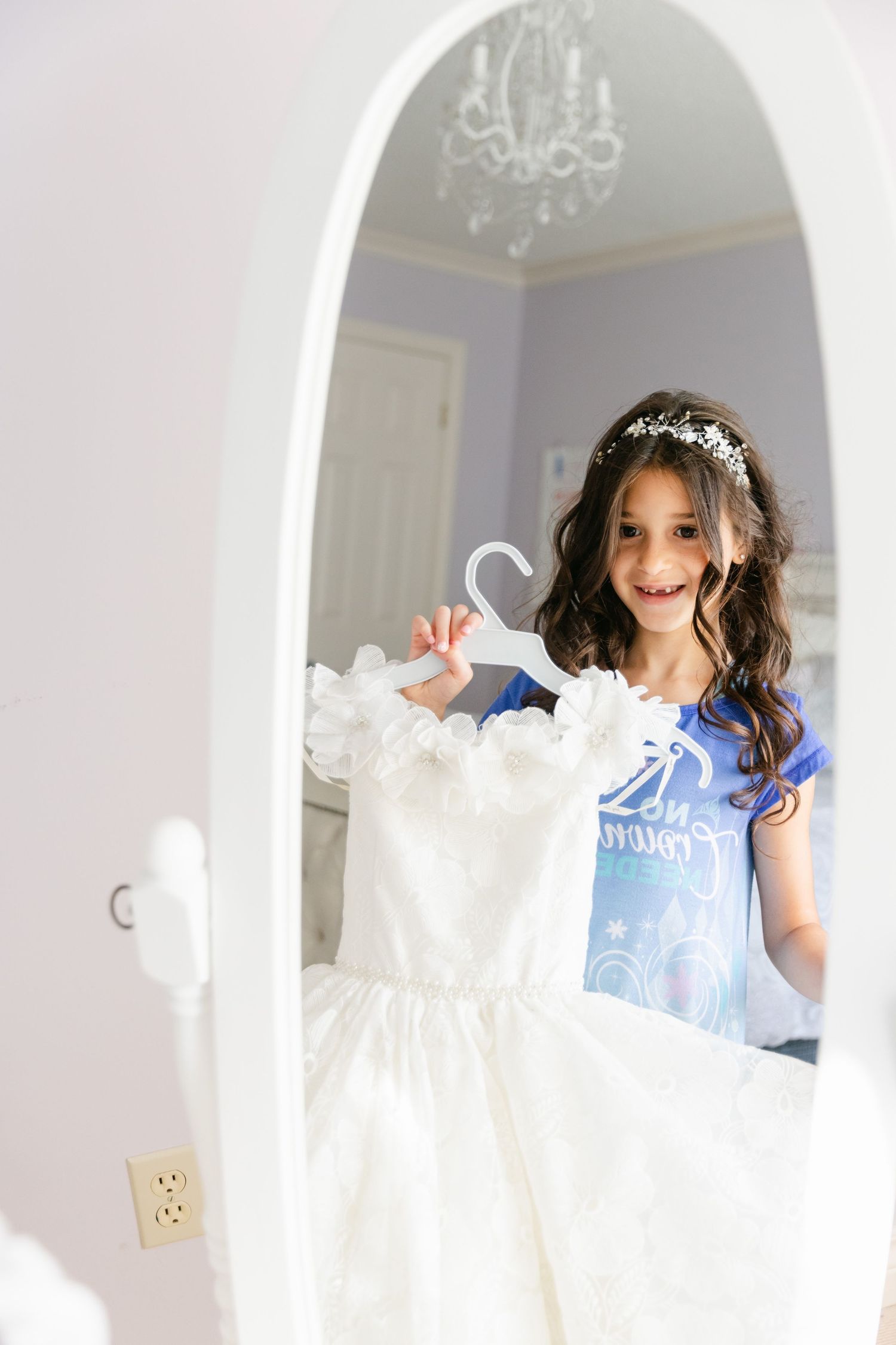 White wedding dress reflected in arched mirror with chandelier visible above.