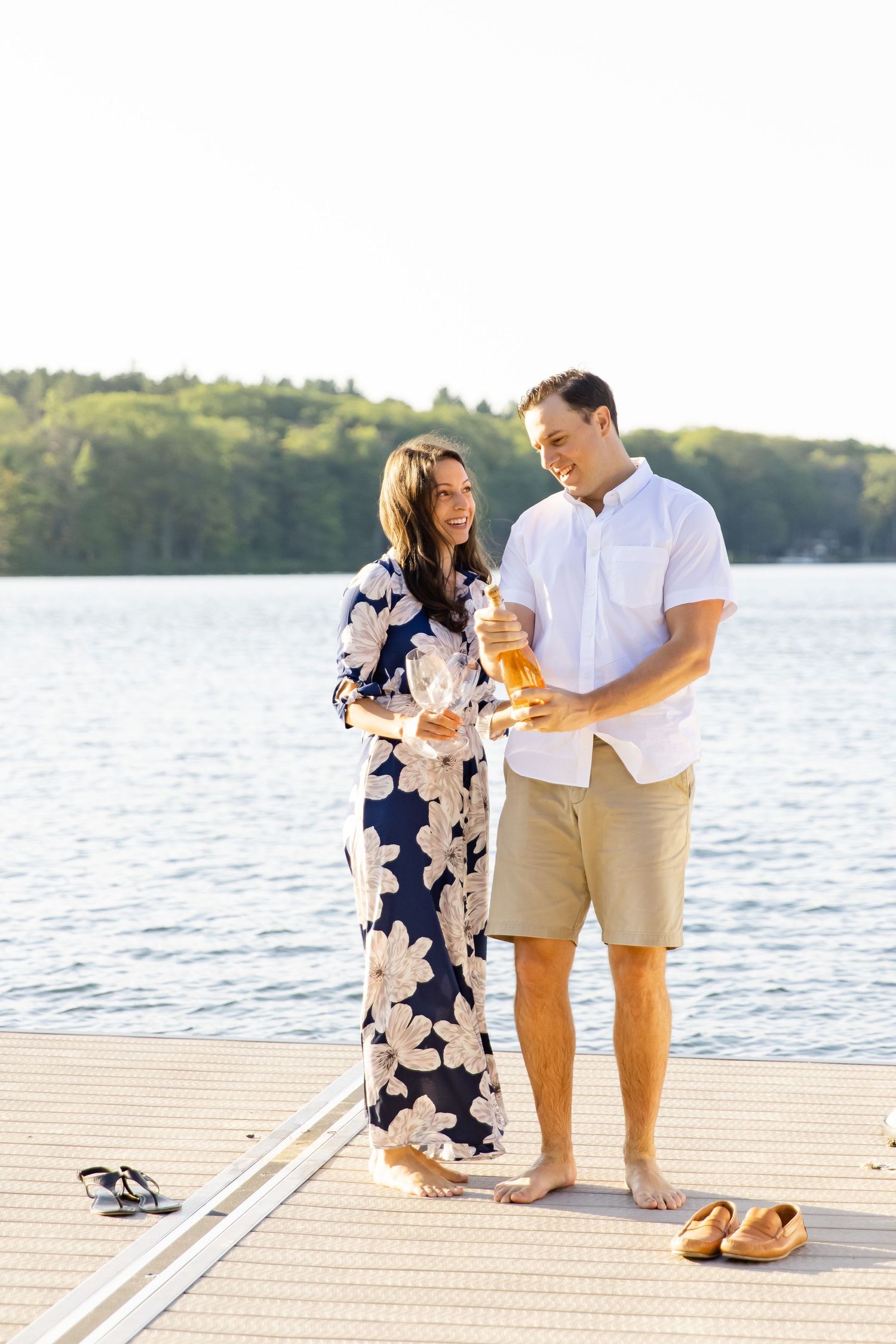 Couple sharing drinks on wooden dock by serene lake in summer.