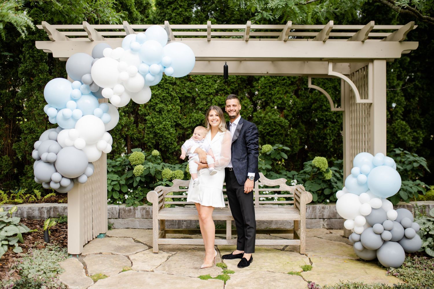 Couple standing under pergola decorated with white and blue balloon arch.