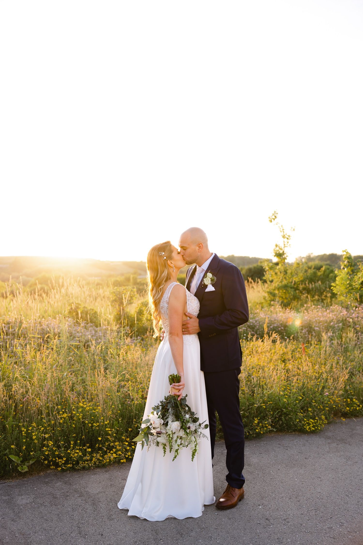 A wedding couple embraces on a path during golden hour surrounded by wildflowers.