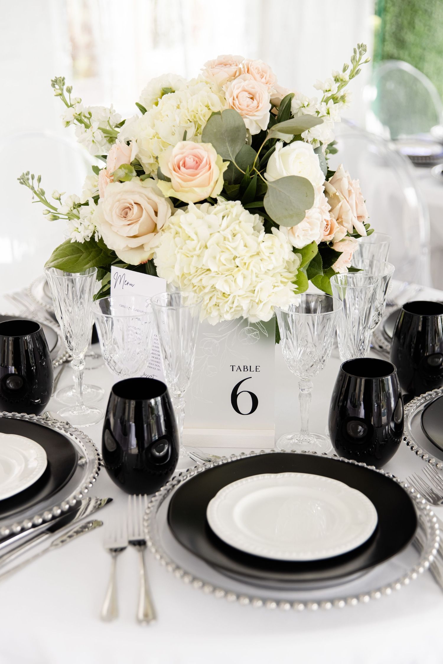 Modern black and white place settings with blush floral centerpiece and table number.
