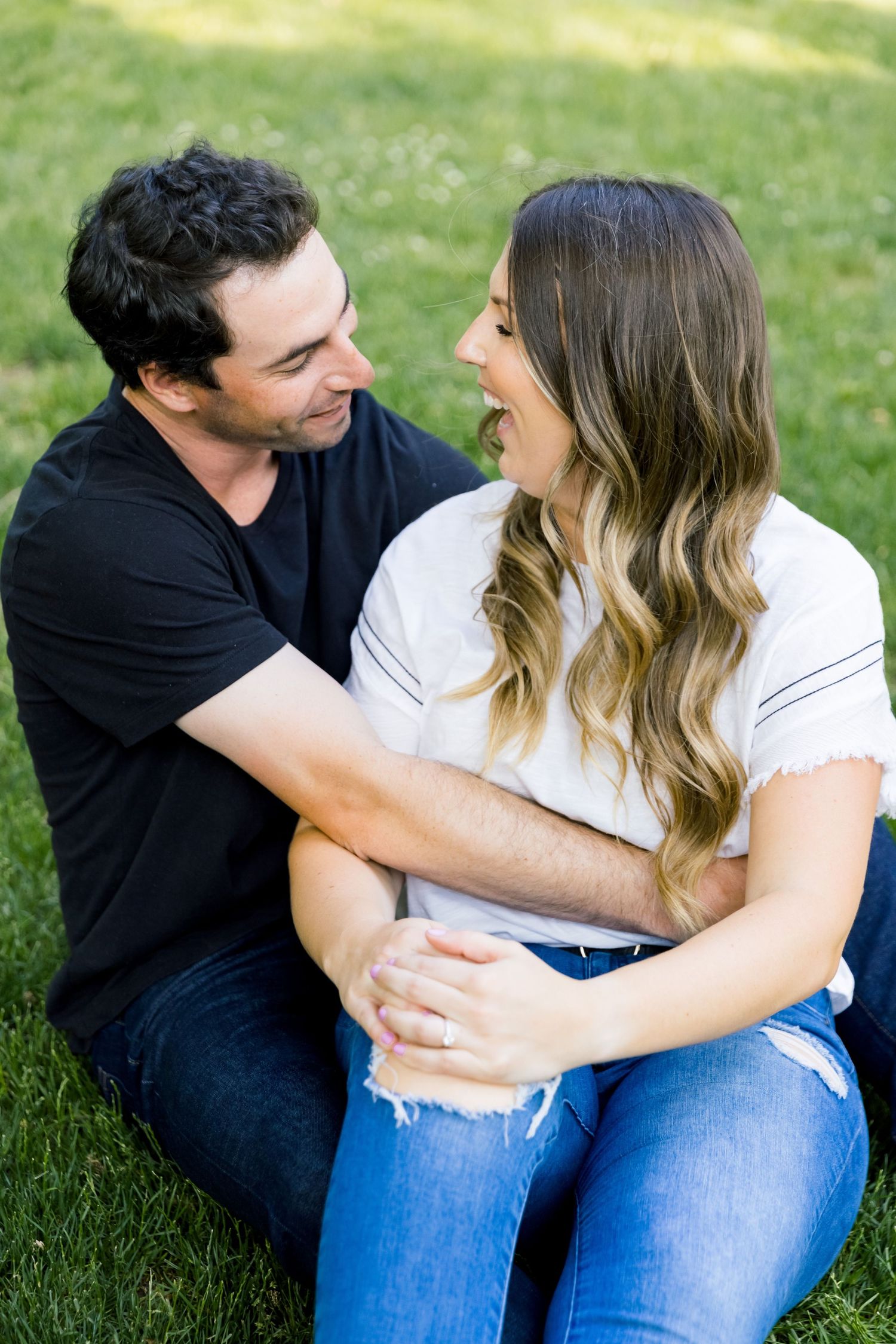 A joyful couple sharing a laugh while sitting together on green grass.